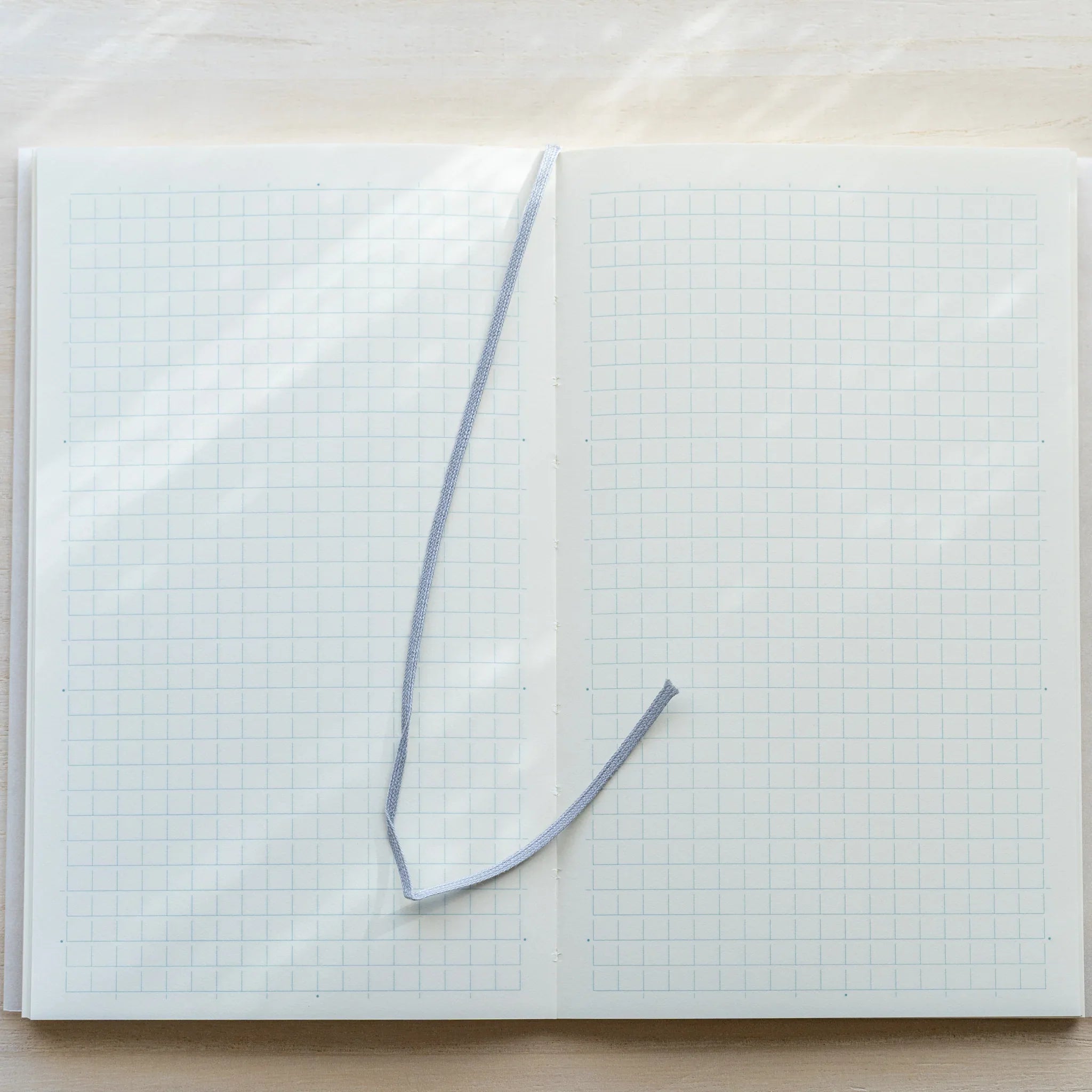 Midori MD Notebook B6 Slim Grid open flat, light blue ribbon bookmark placed diagonally across white grid pages
