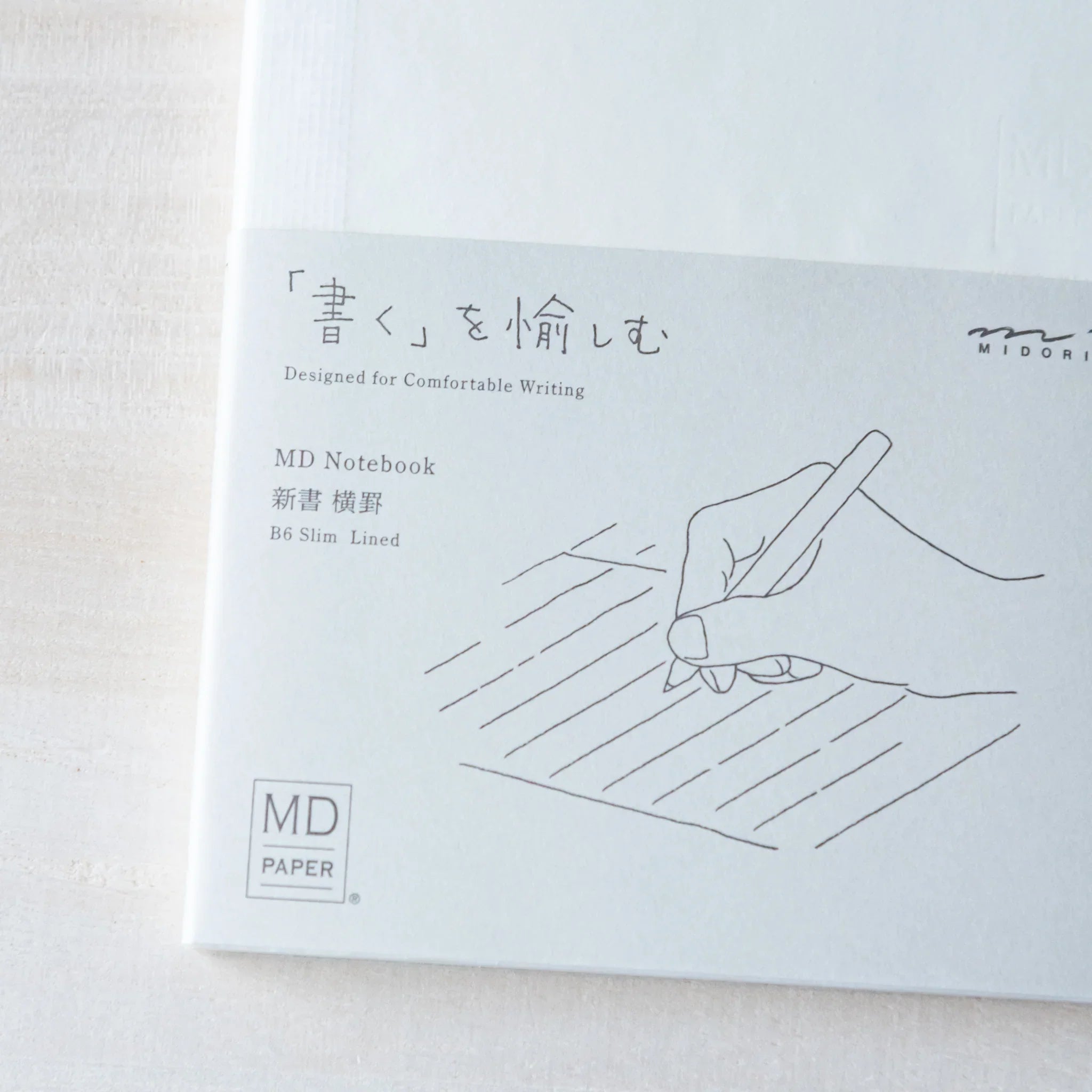 Japanese Notebook front view of a Midori MD B6 notebook with a paper band featuring a hand-drawn writing illustration.