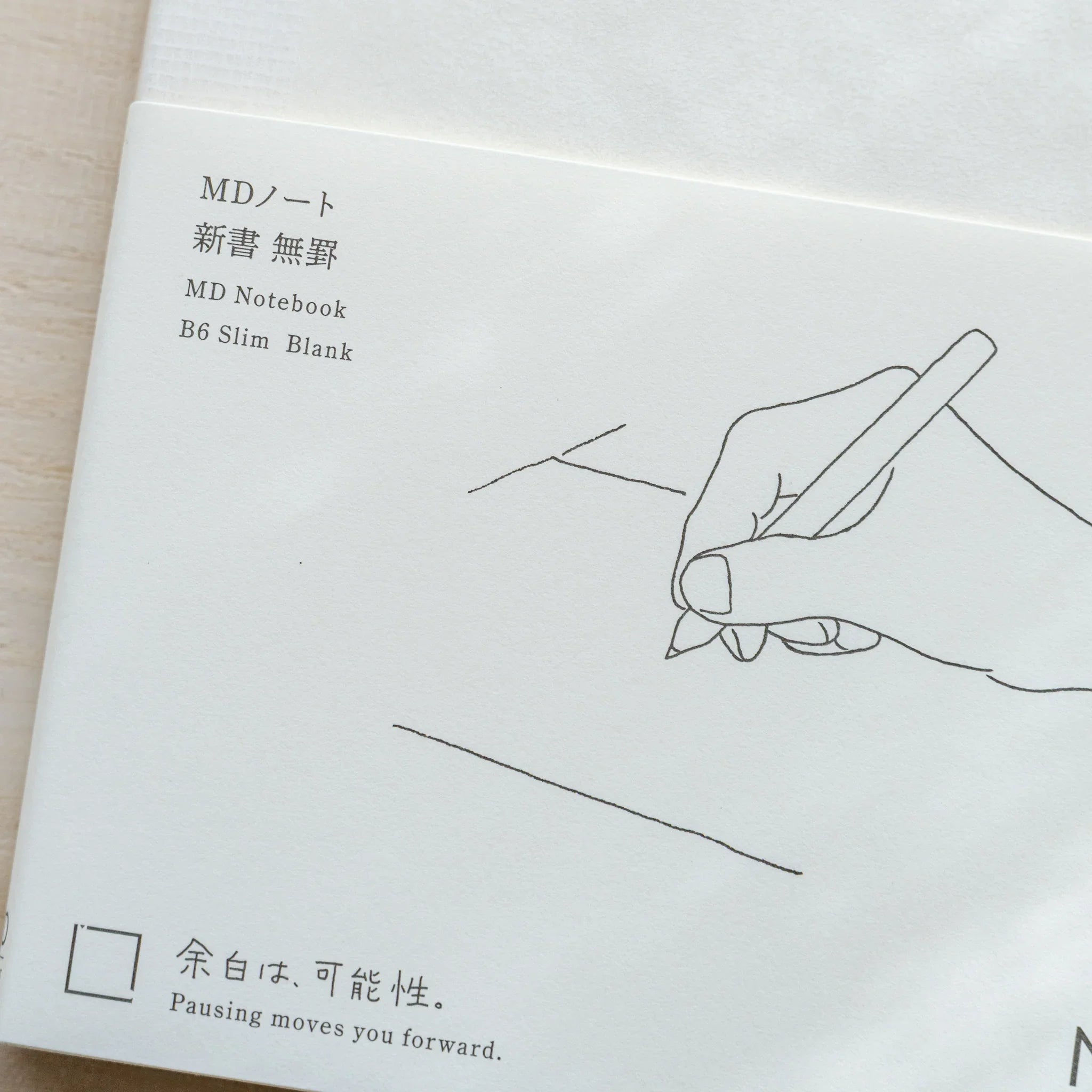 Close-up of Midori MD Notebook B6 Slim Blank cover showing hand and pen illustration, Japanese and English product name text