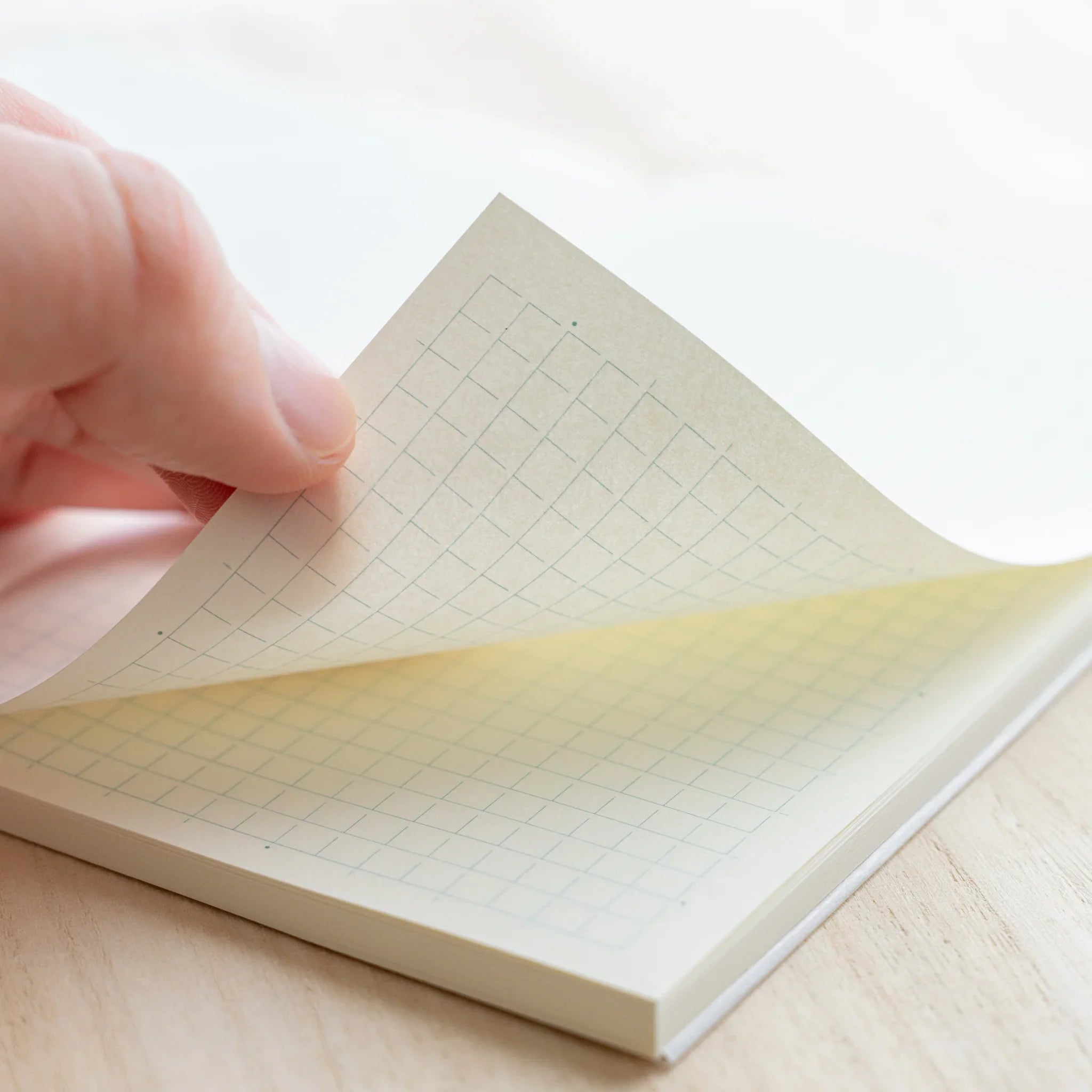 Hand turning a page of Midori MD Notebook B6 Slim Grid showing light blue grid on ivory paper and cloth-bound spine corner