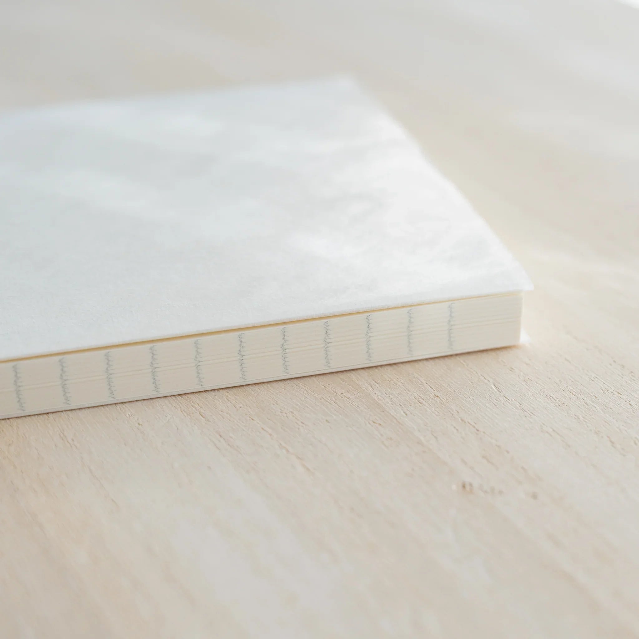Midori MD Notebook B6 Slim side view showing white cover, ivory page edges, and visible thread binding stitching on spine