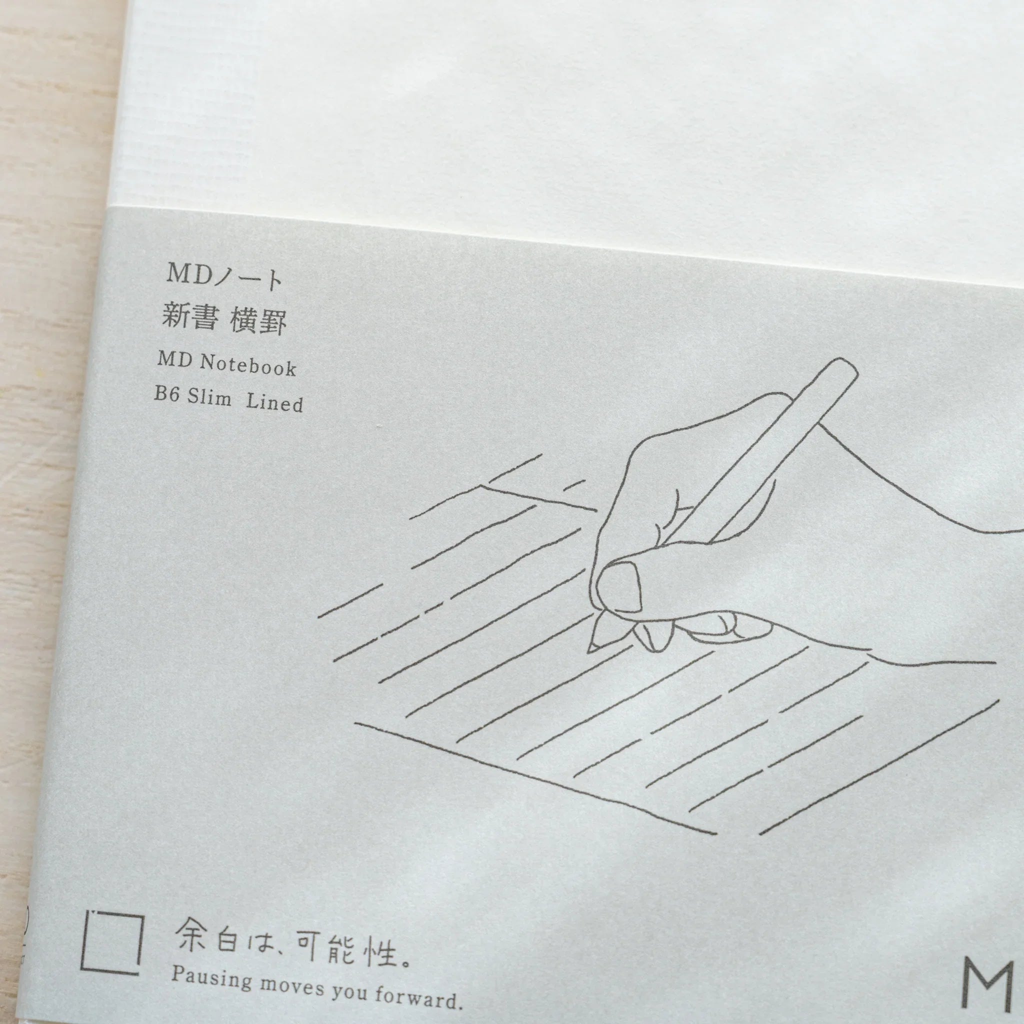 Close-up of Midori MD Notebook B6 Slim Lined gray cover with hand on lines illustration, Japanese and English text labels