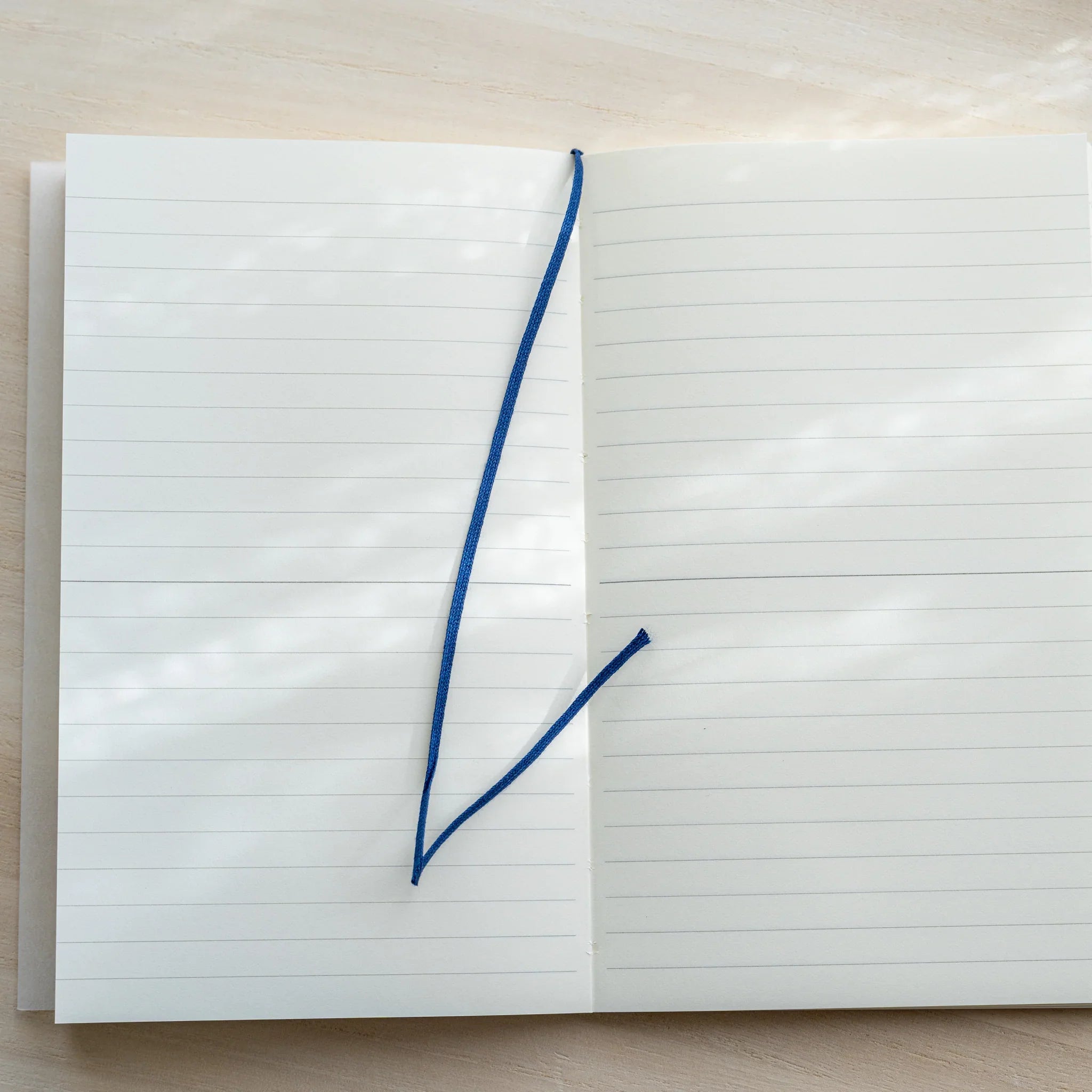 Midori MD Notebook B6 Slim Lined open flat, blue ribbon bookmark laid diagonally across white lined pages