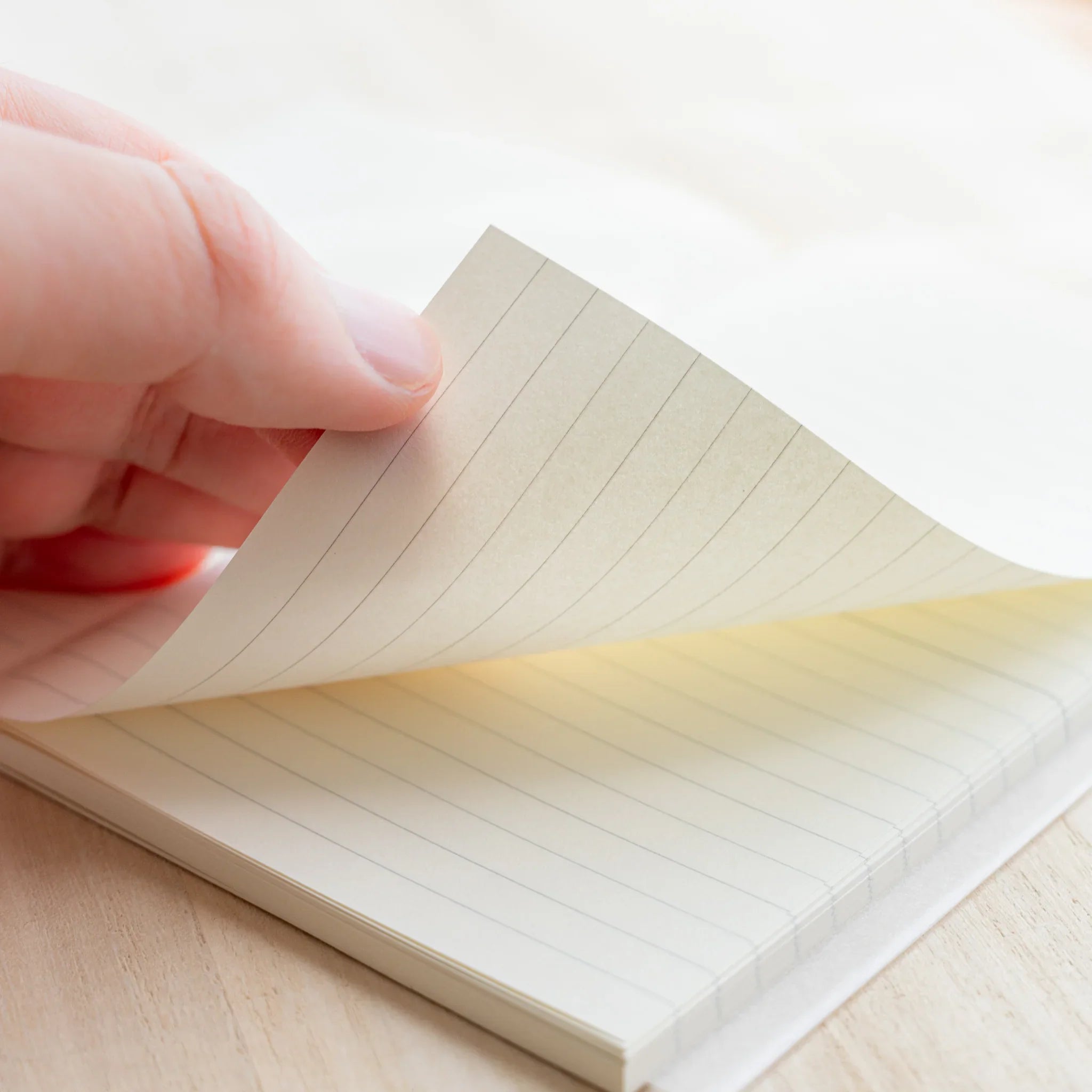 Hand turning a page of Midori MD Notebook B6 Slim Lined, showing ivory paper thickness and gray lined pattern