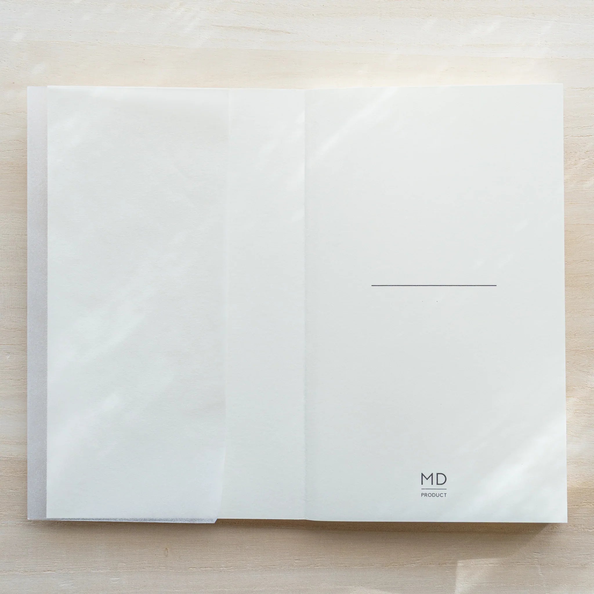 Midori MD Notebook B6 Slim open flat showing glassine inner cover on left and first white page with MD PRODUCT logo on right