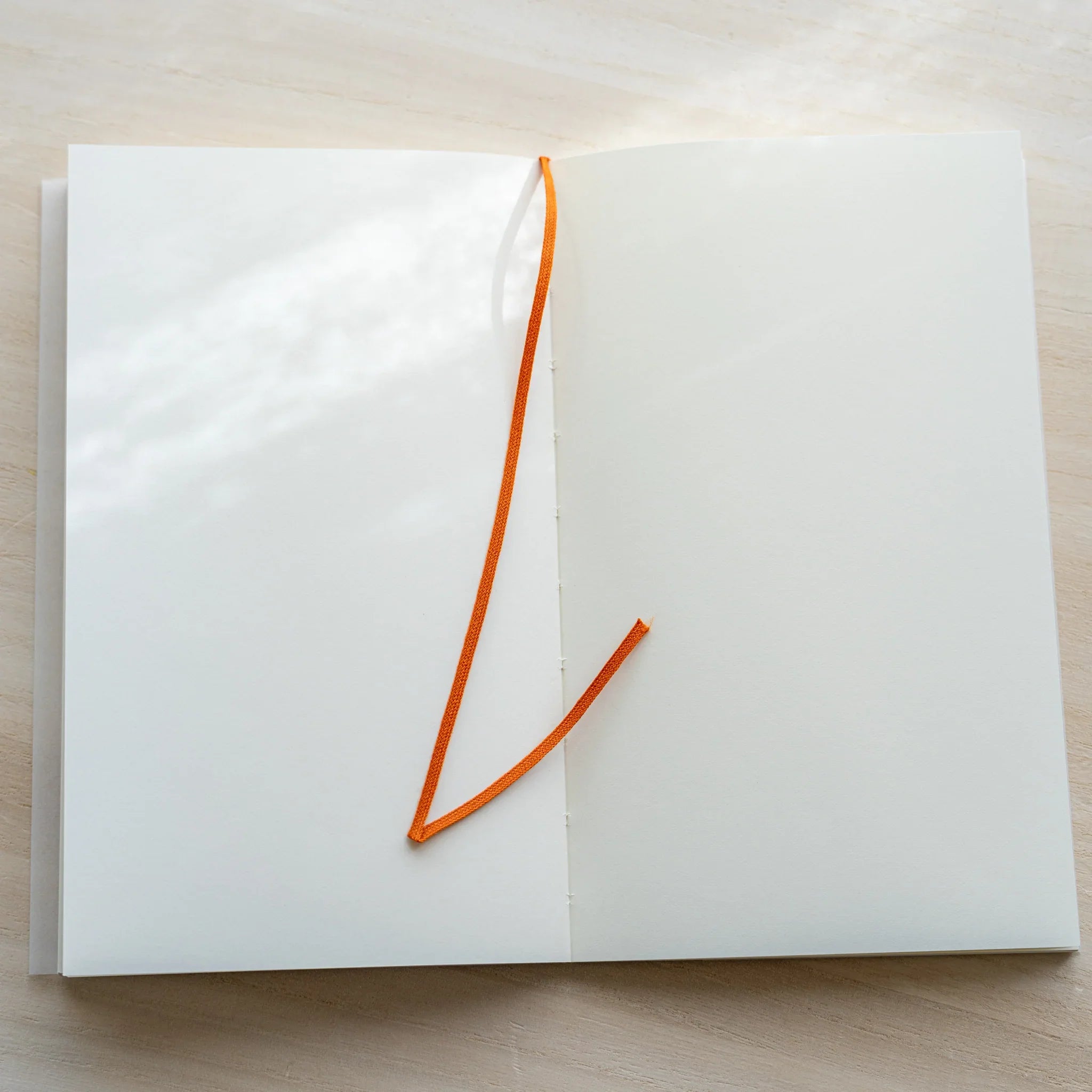 Midori MD Notebook B6 Slim Blank open flat with orange bookmark ribbon hanging across blank white pages and center spine