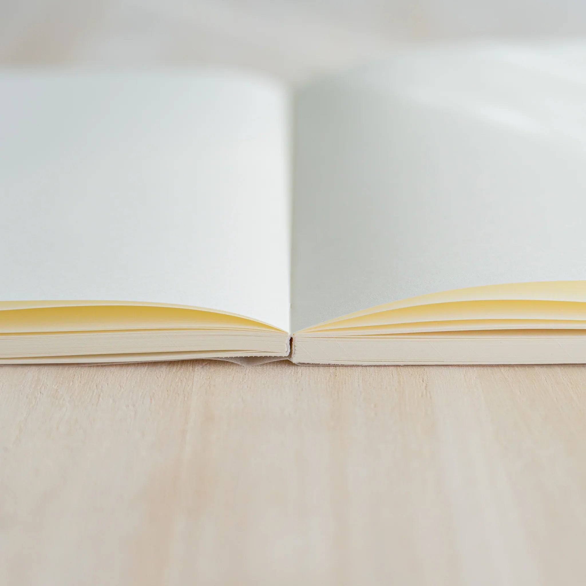 Side view of Midori MD Notebook B6 Slim Blank open, showing cream page edges and thread-stitched binding on light wood