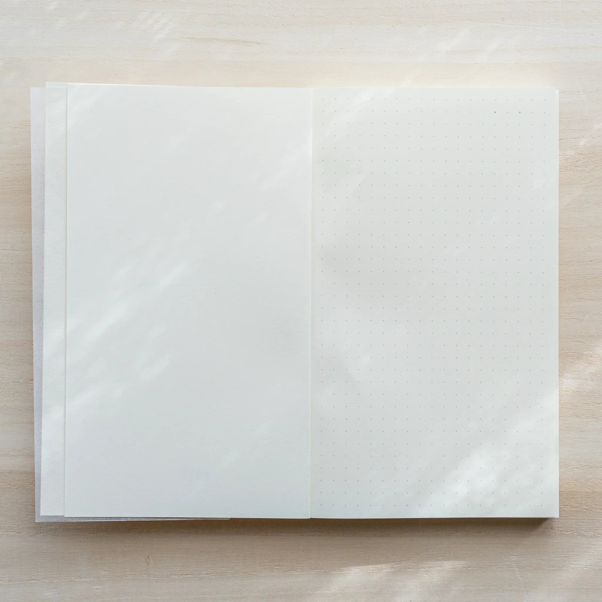 Midori MD Notebook B6 Slim open flat, glassine inner cover on left, ivory dot grid page on right, flat-lay on light wood