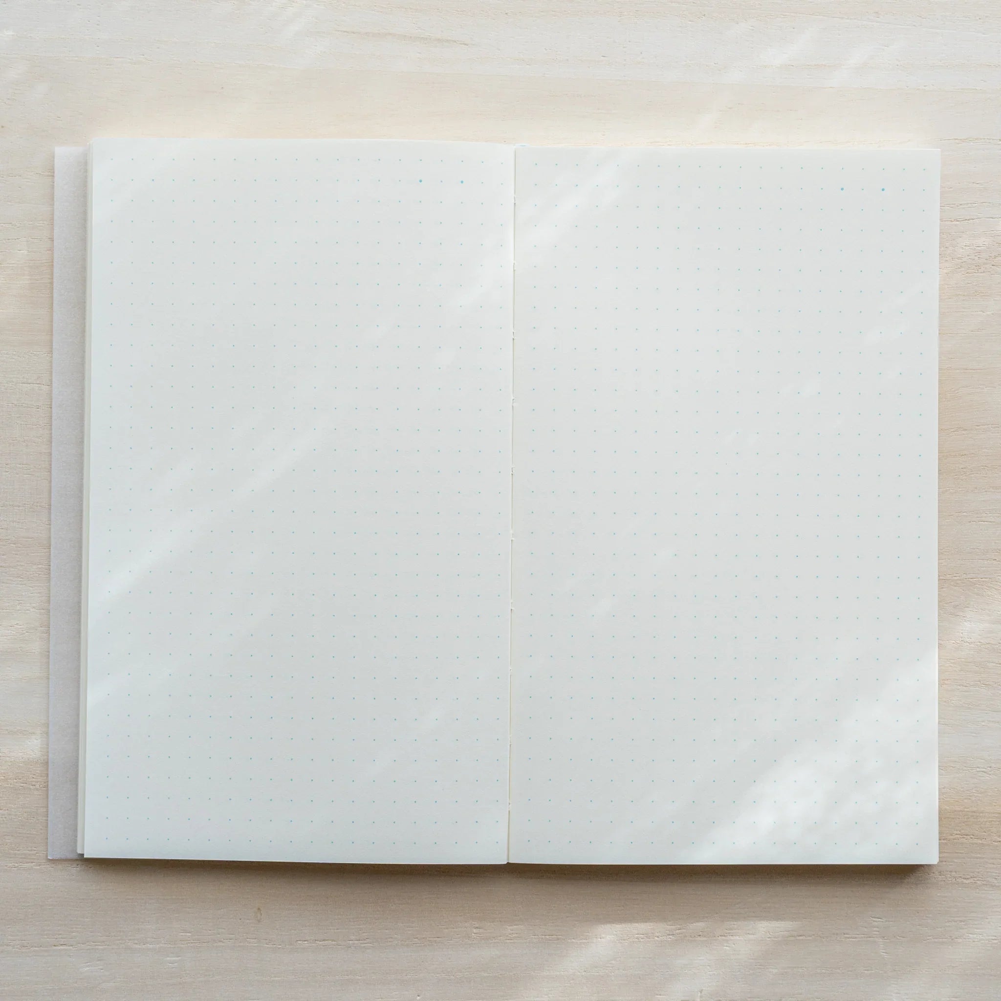 Midori MD Notebook B6 Slim open flat to dot grid spread, ivory pages, flat-lay on light wood surface