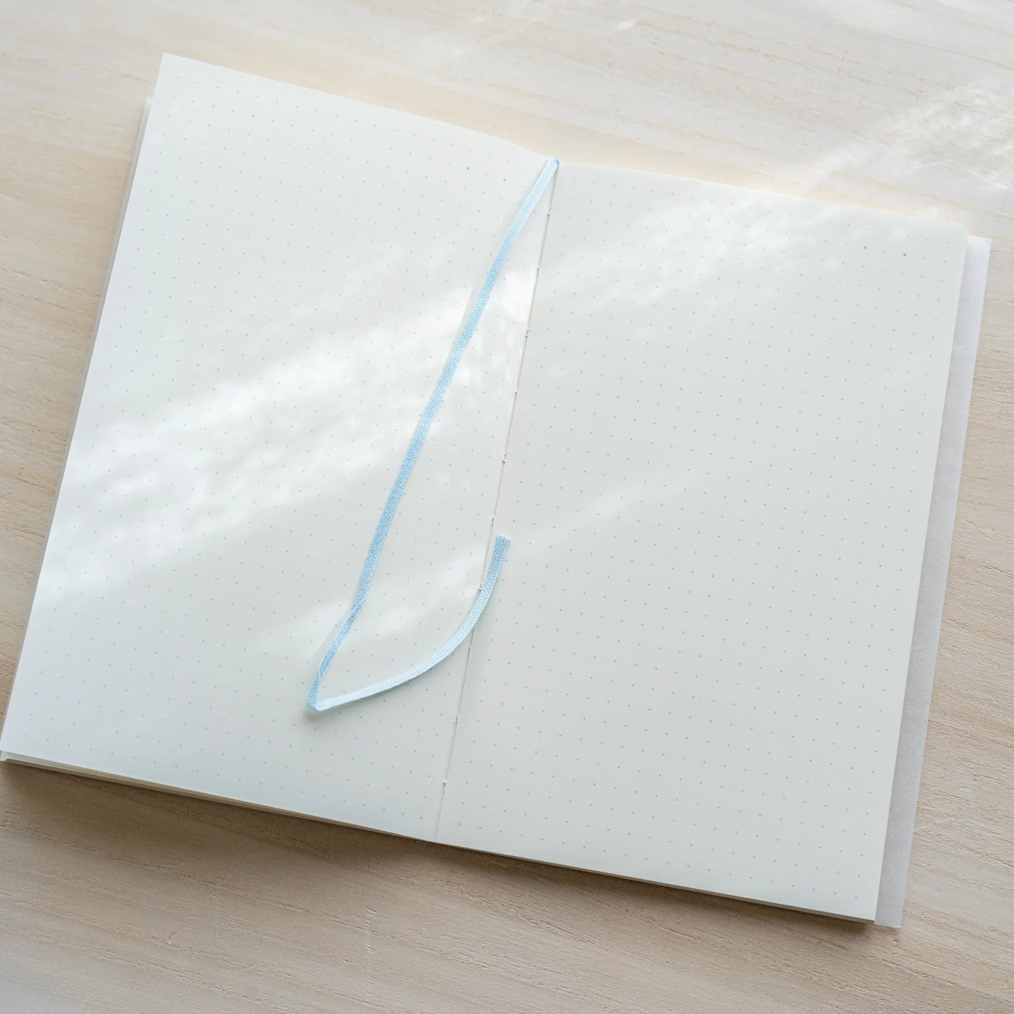 Midori MD Notebook B6 Slim open flat showing light blue bookmark ribbon and ivory dot grid pages on light wood