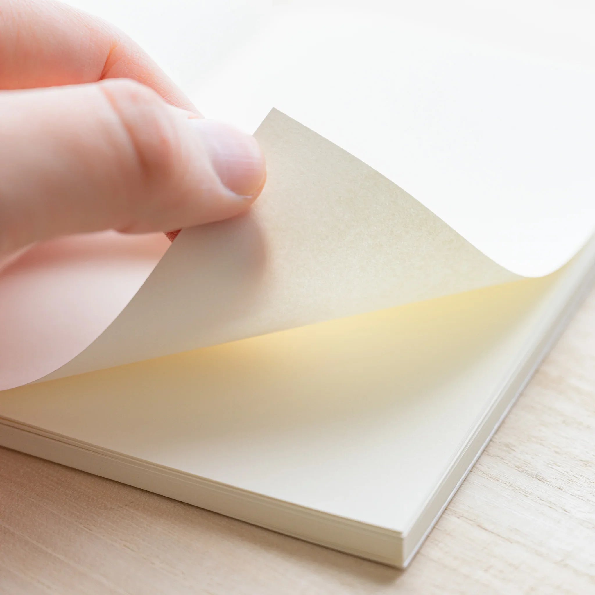 Hand peeling back a page of Midori MD Notebook B6 Slim, showing ivory paper and page thickness, on wood surface