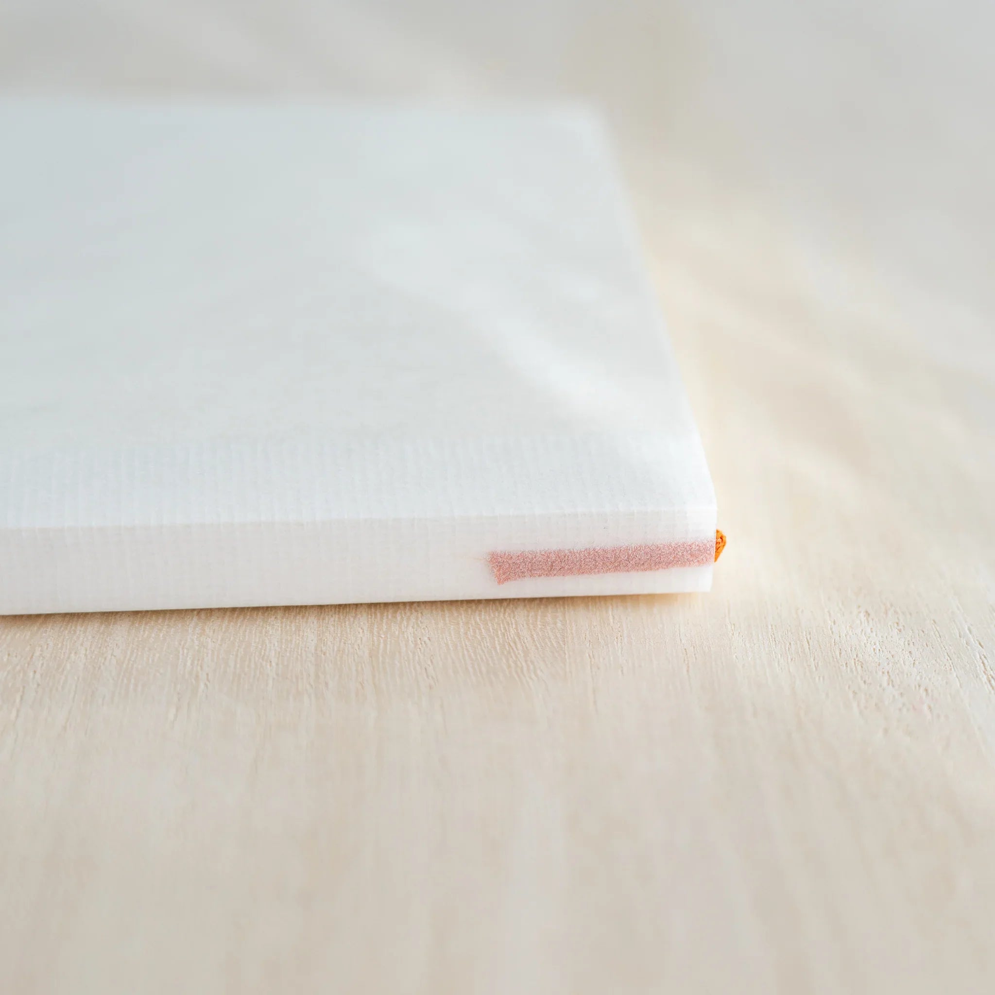 Midori MD Notebook B6 Slim side view, white cover, ivory page edges with orange ribbon bookmark at corner, on wood surface