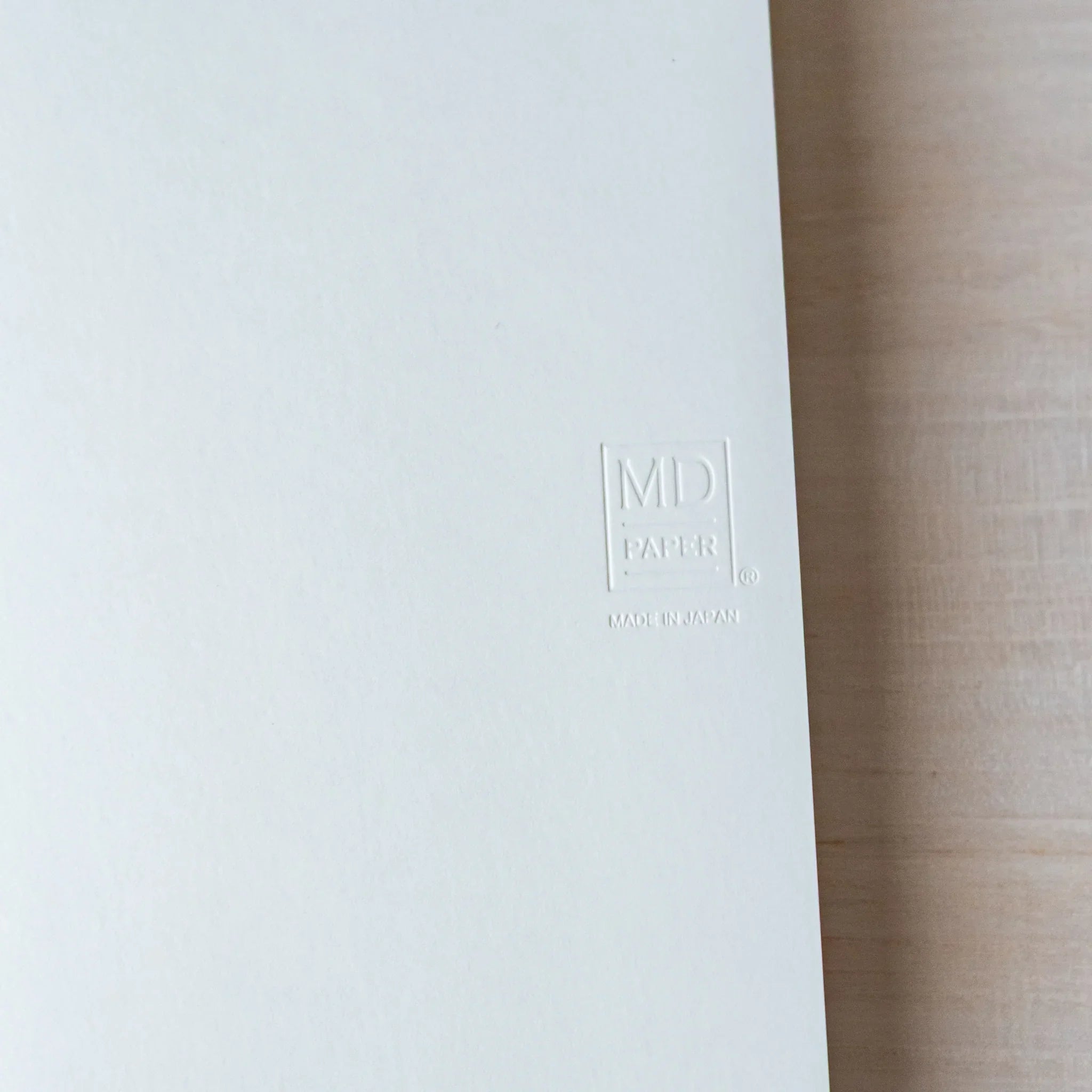 Japanese Notebook cover close-up of a Midori MD B6 notebook, featuring an embossed MD PAPER logo on a minimalist white surface.