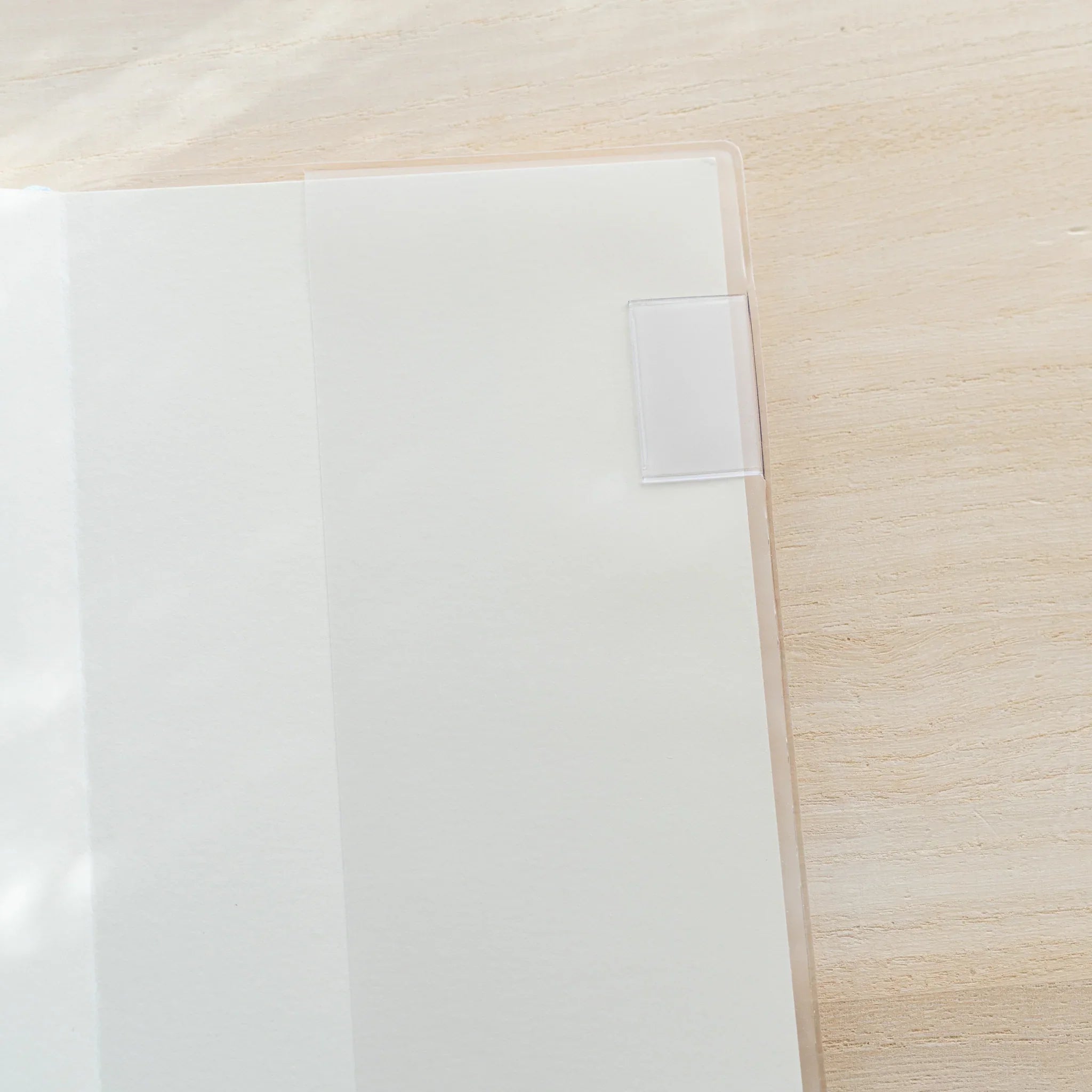 Close-up of MD Notebook Cover top-right corner showing white plastic bookmark tab and clear PVC cover edge on wooden surface