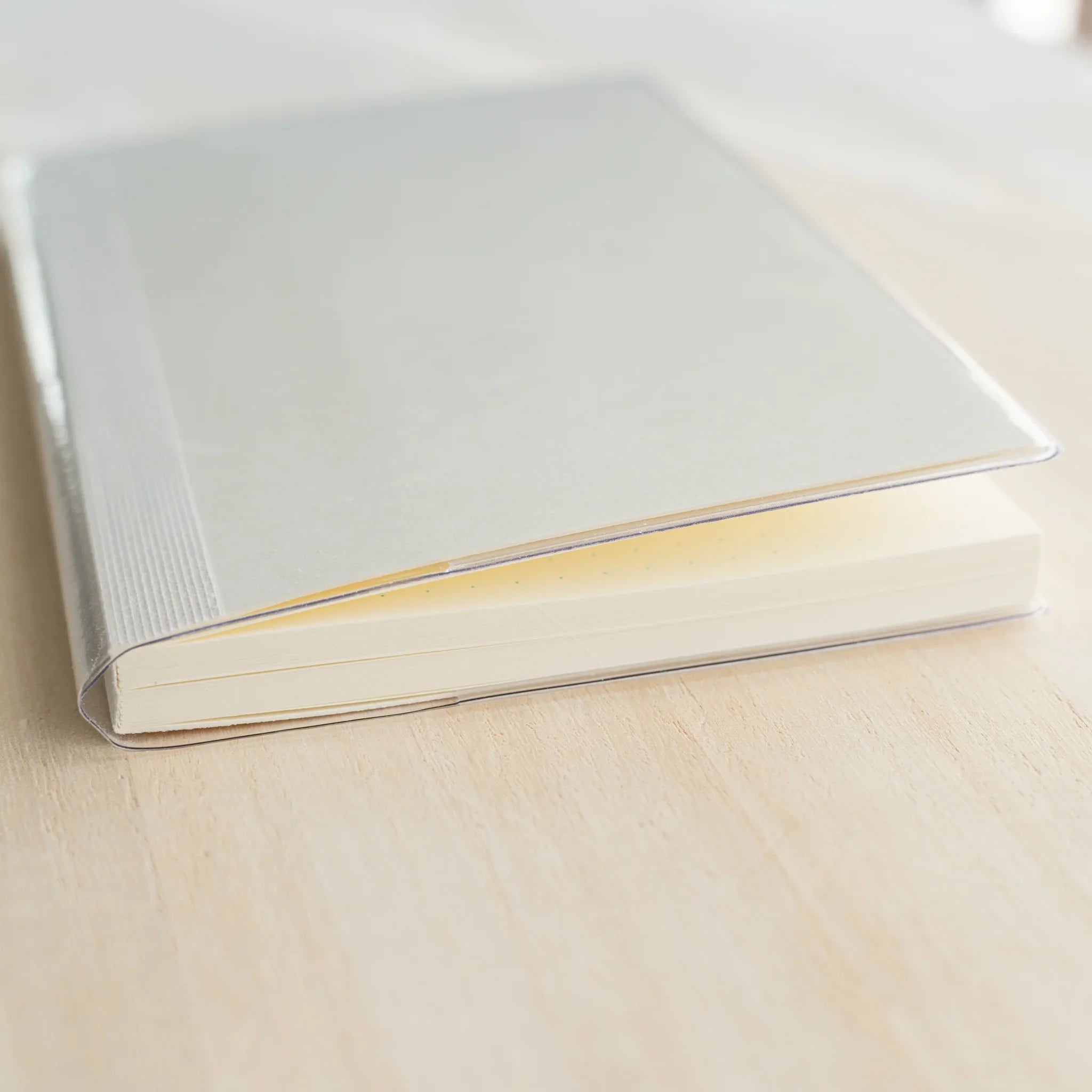 Side view of Midori MD Notebook inside clear PVC cover showing ivory page edges, white ribbed cloth spine, and clear PVC edge