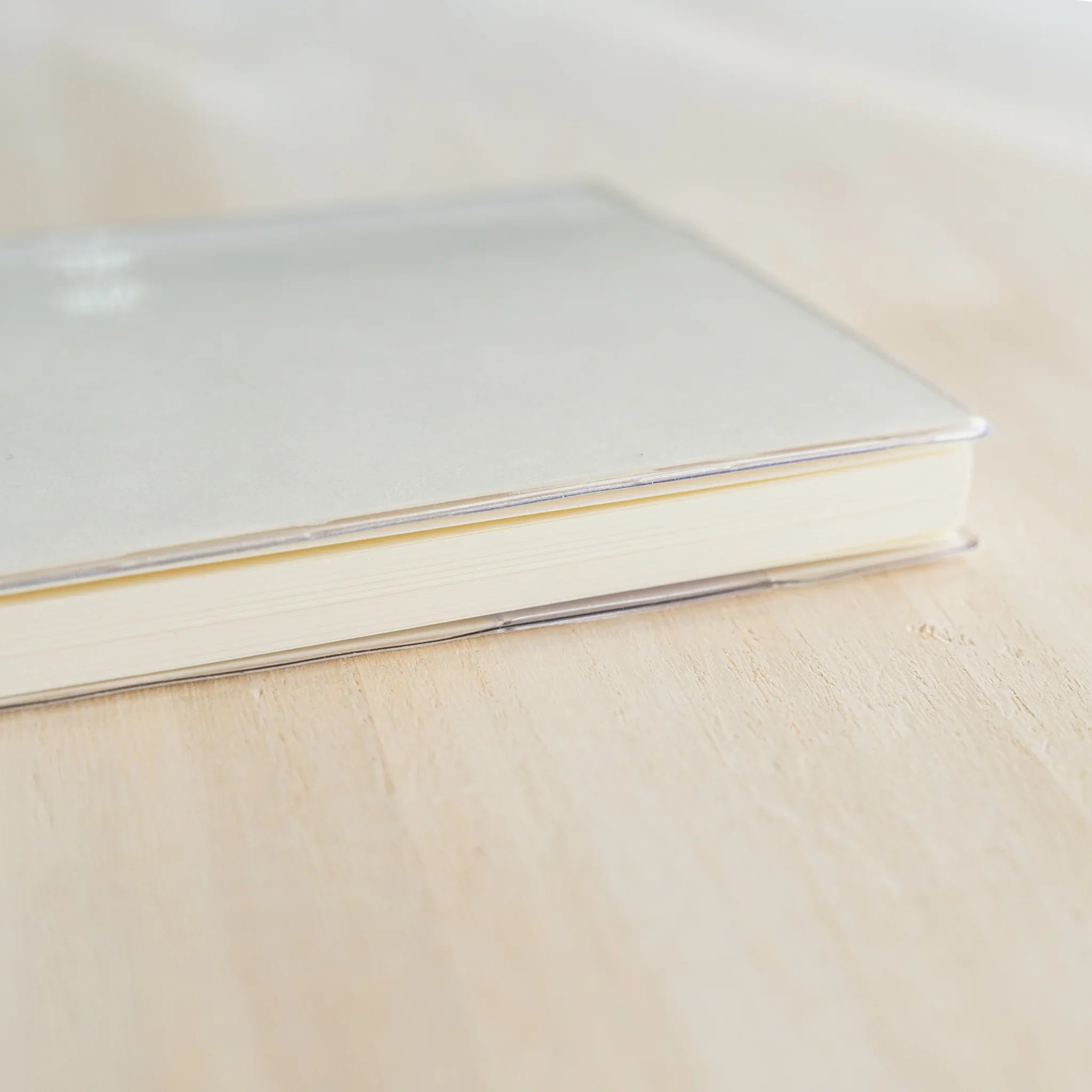 Close-up of Midori MD Notebook Cover top edge showing clear PVC rim and ivory page edges on wooden surface