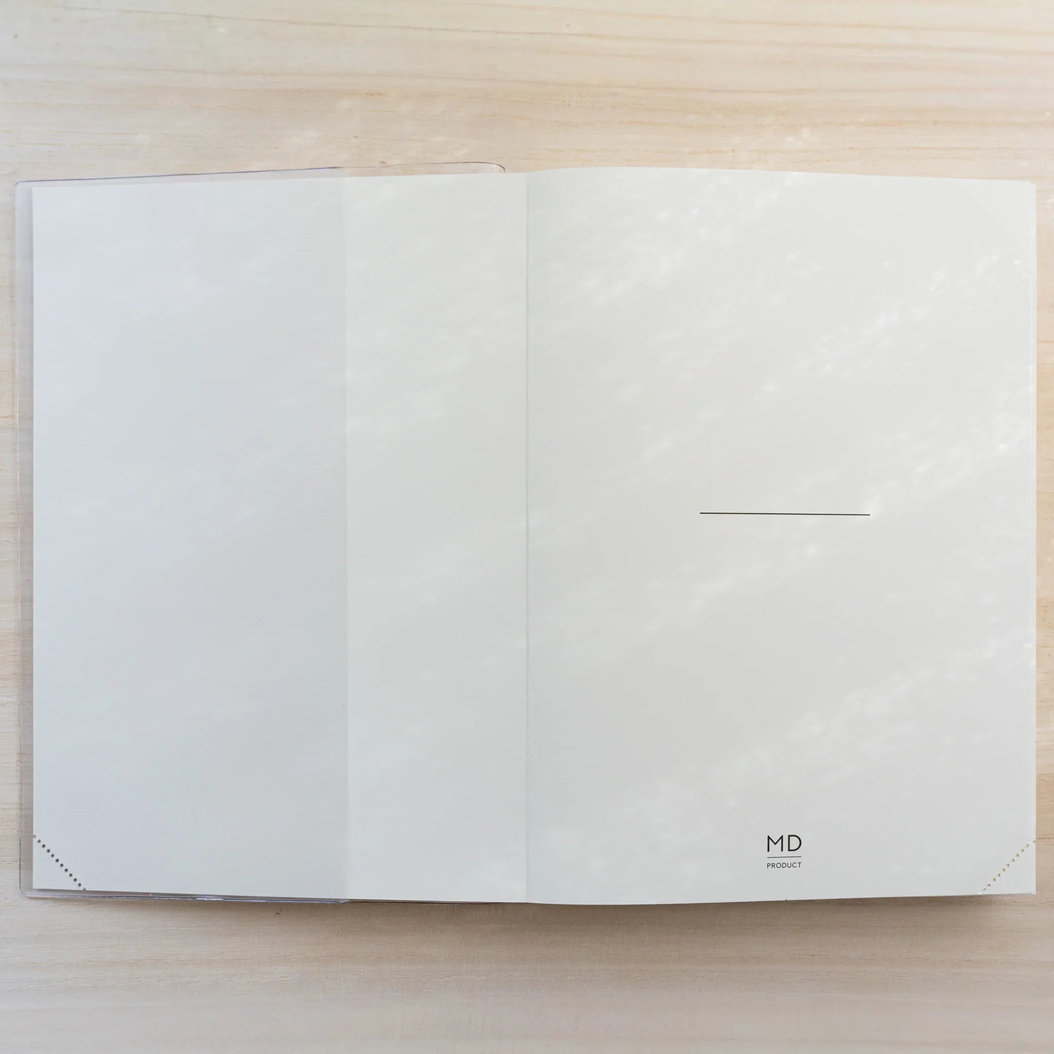 Midori MD Notebook Cover open flat in clear PVC showing a blank ivory-white spread and center fold