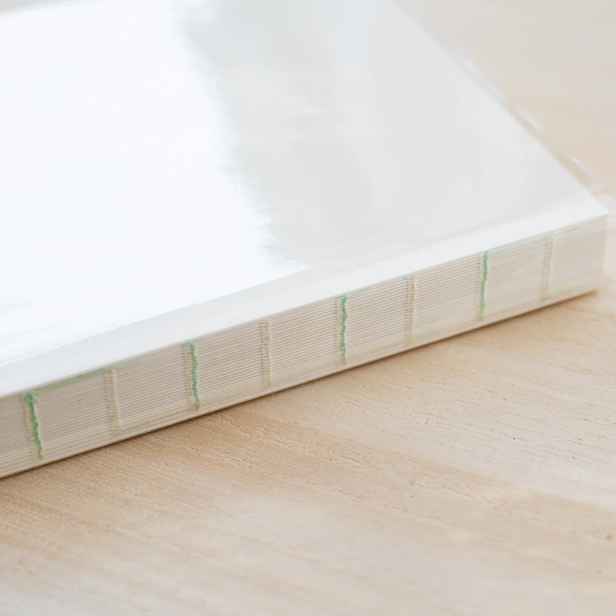 Close-up of an MD notebook page block edge showing green thread binding under a clear PVC cover