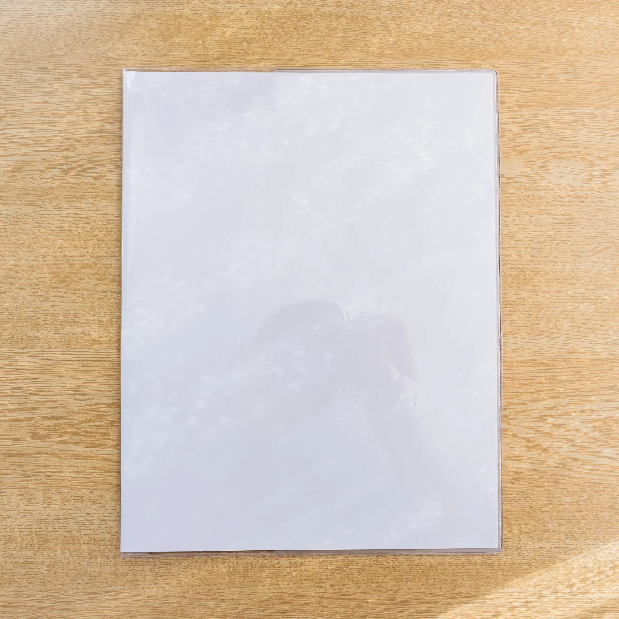 Clear PVC Midori MD Notebook Cover over a white MD notebook, closed front view on a wood surface