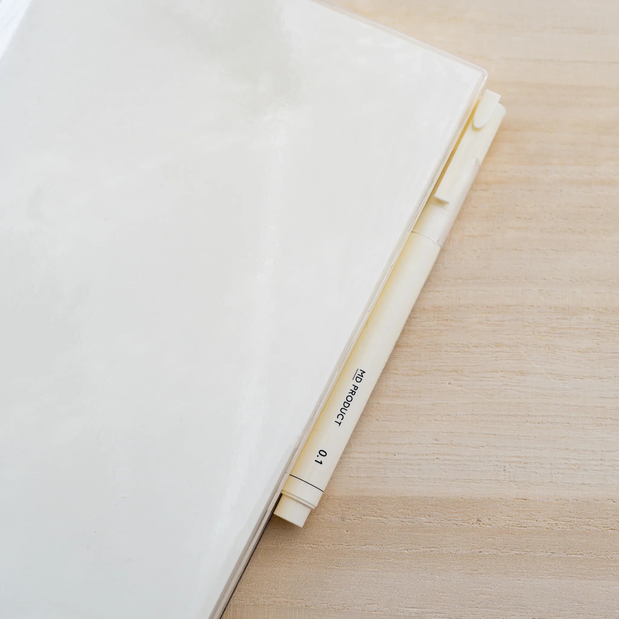 Side view of a thick MD notebook inside a clear PVC cover on a wood surface