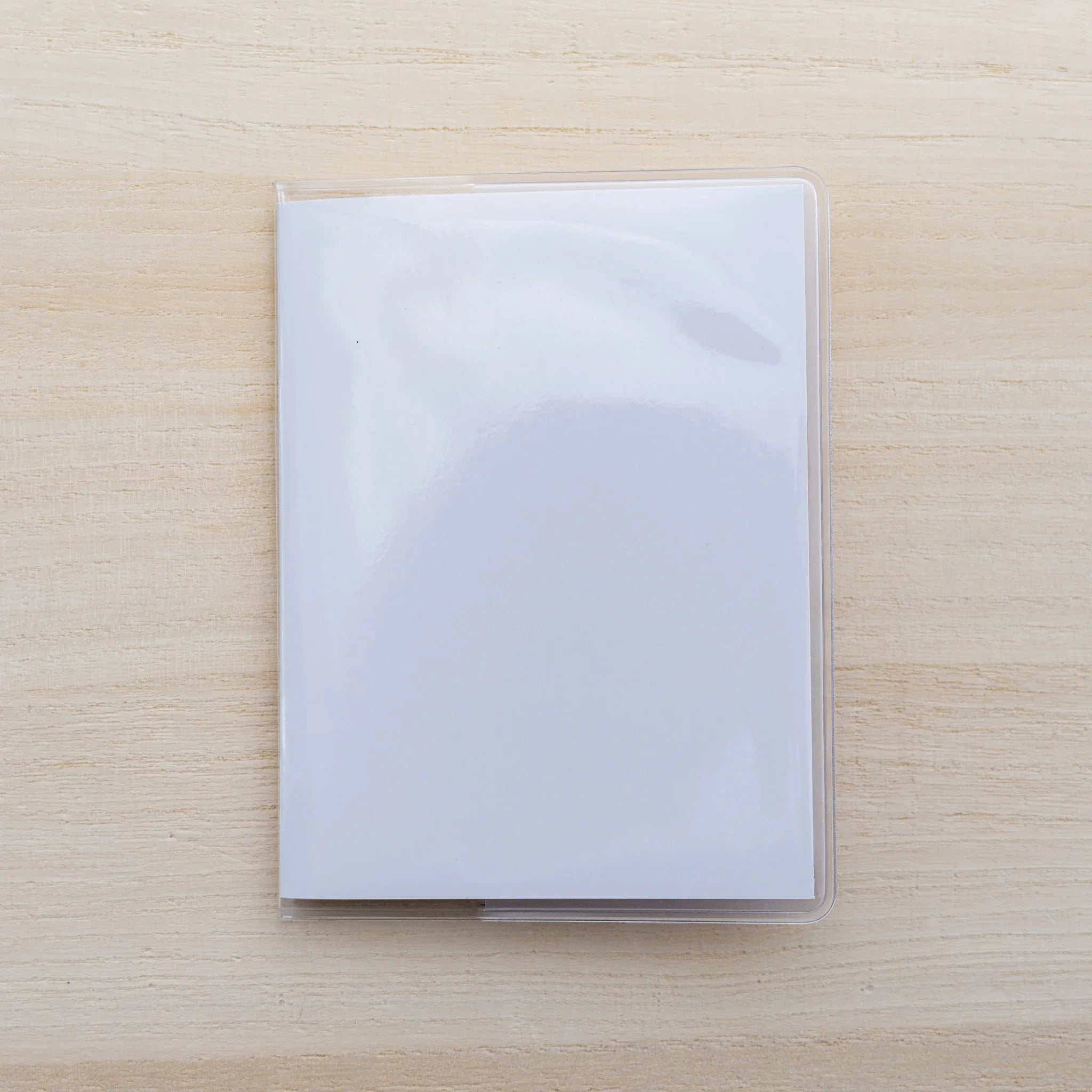 Clear glossy vinyl MD Notebook Cover over a plain white notebook, front view on a wood surface