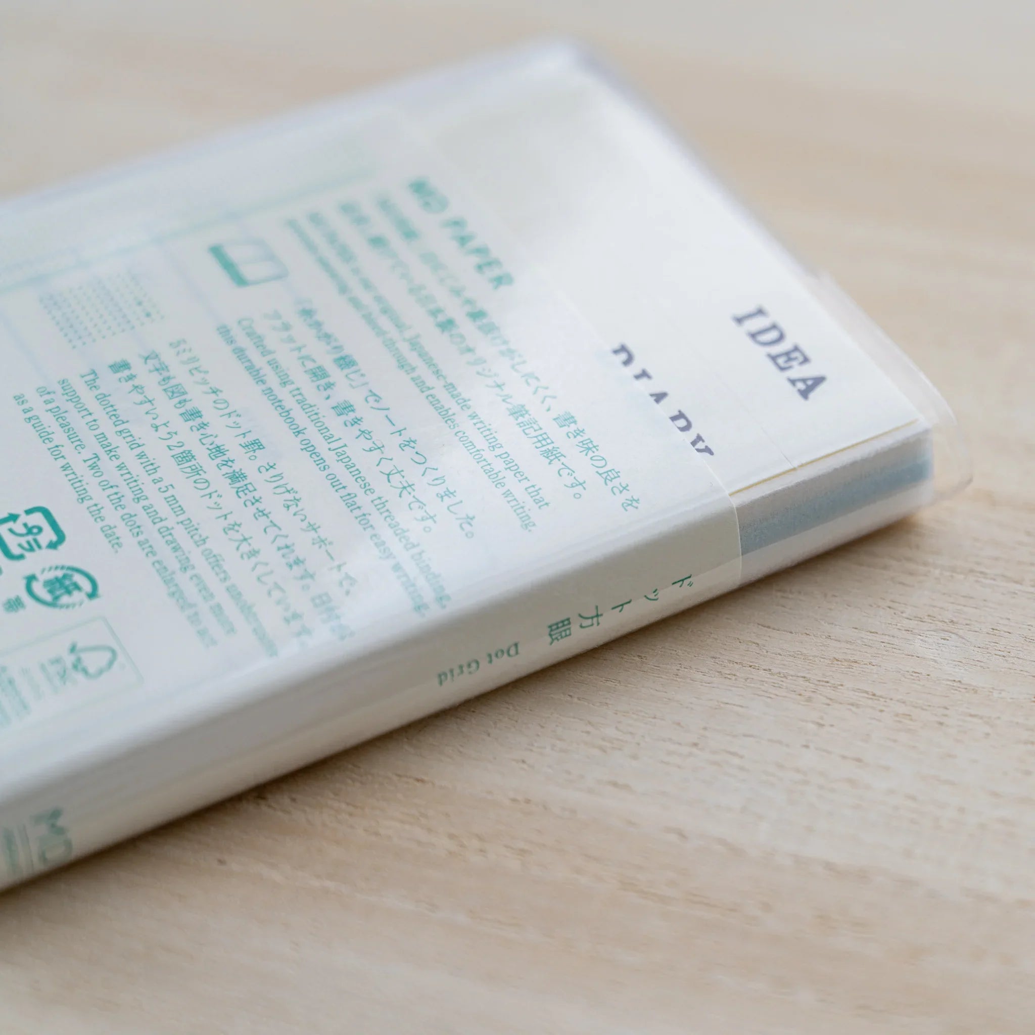 Close-up of a clear vinyl cover over an MD Notebook showing green MD Paper text and dot grid description, on wood
