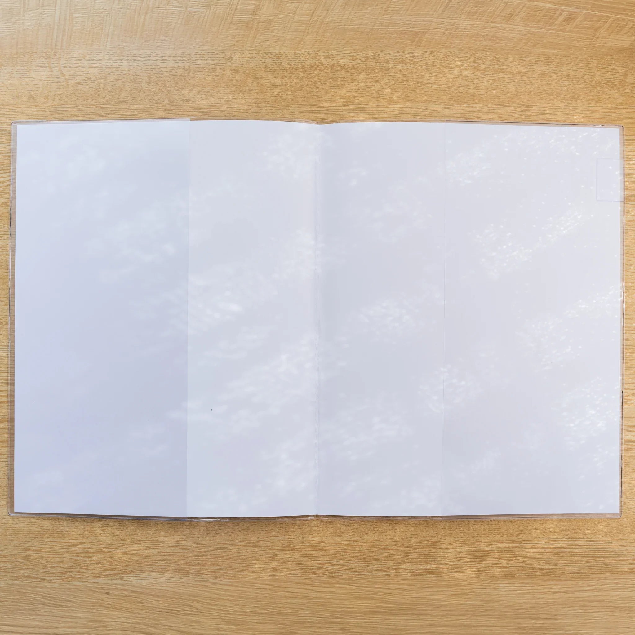 Midori MD Notebook Cover opened flat in clear PVC showing blank white inner-cover panels and a white page