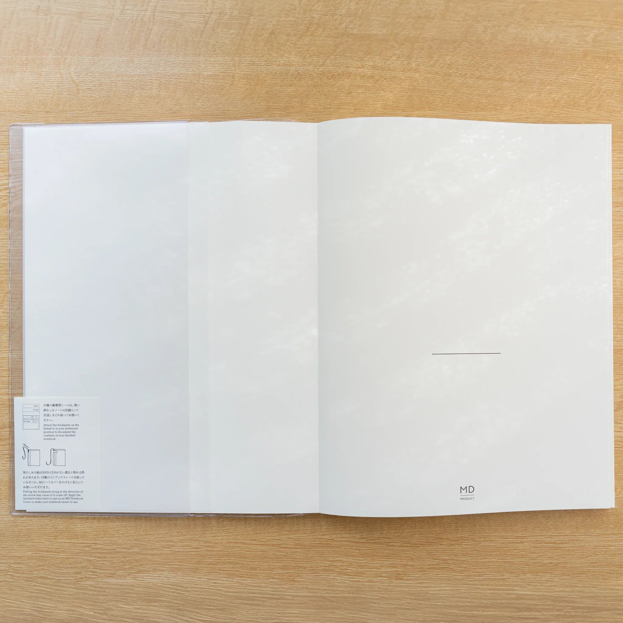 Midori MD Notebook Cover opened flat over a notebook in clear PVC, blank white spread on a wood surface