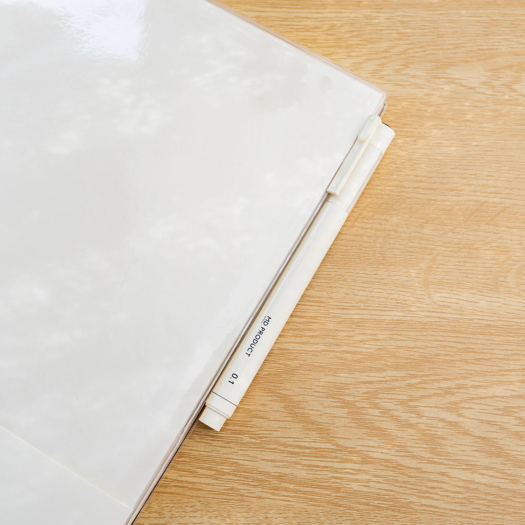 Angled view of clear PVC Midori MD Notebook Cover on a notebook with a clip ruler at the top edge