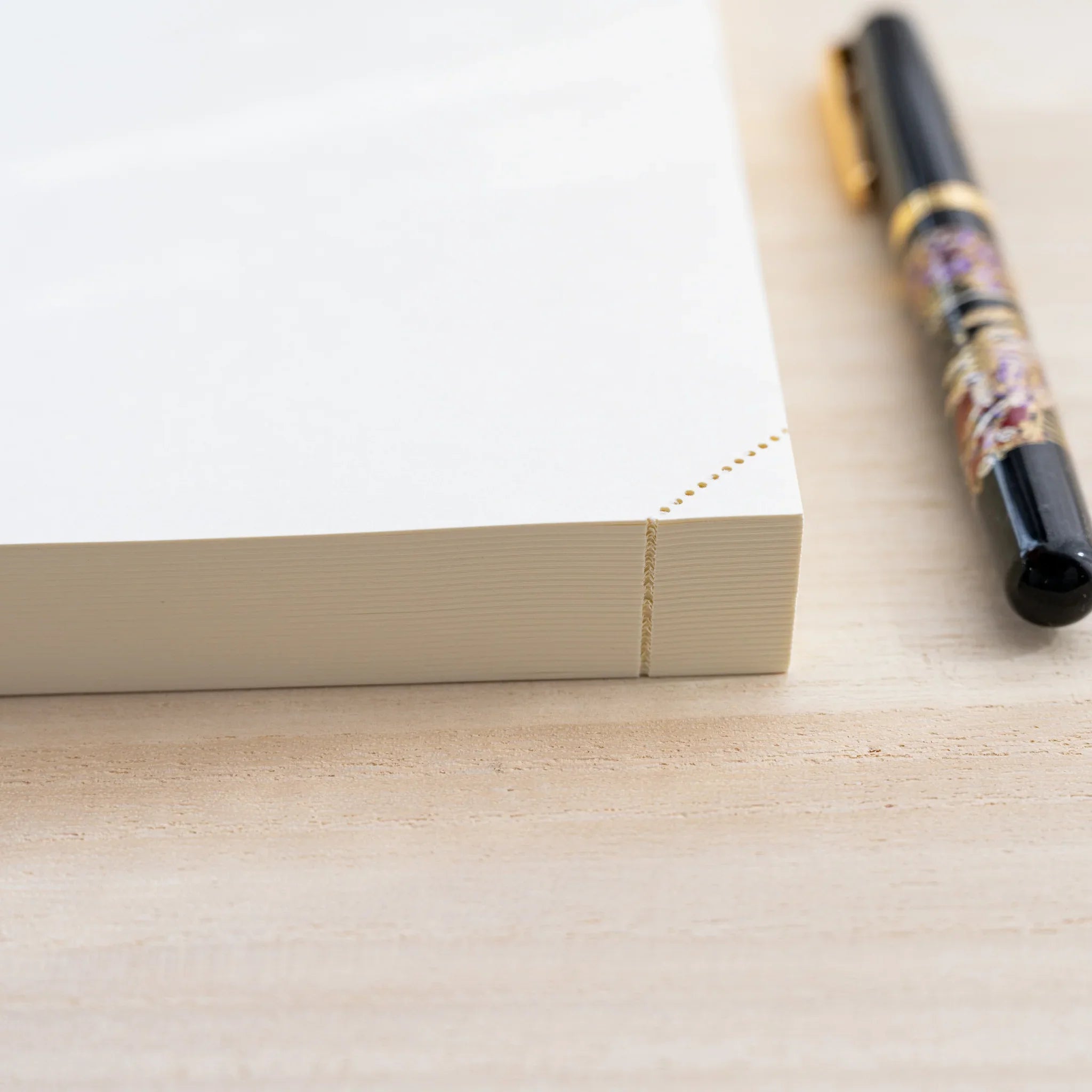Closed Midori MD Notebook at an angle showing thick cream page block and gold corner dots, black fountain pen beside