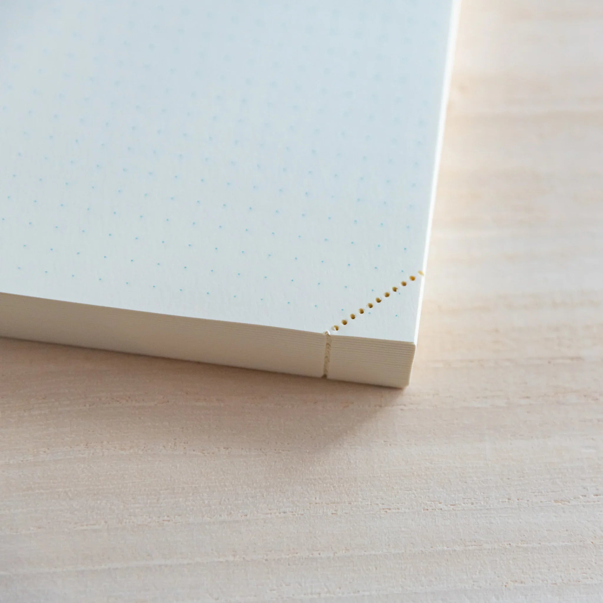 Close-up of Midori Japanese journal corner with dot grid pages and perforated tear-off corner on light wood.