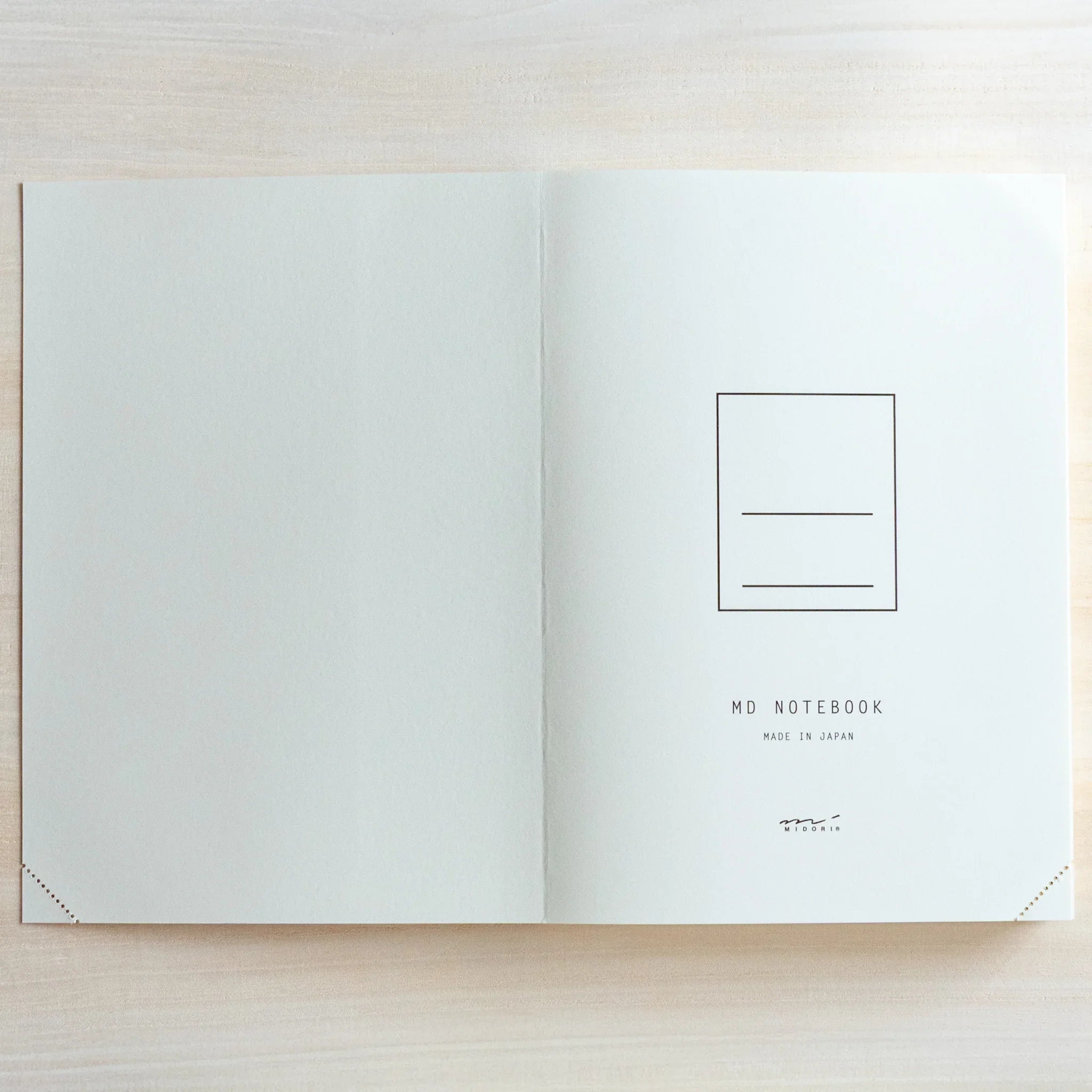 Top view of open Midori Japanese journal showing blank double-page spread on light wood surface.
