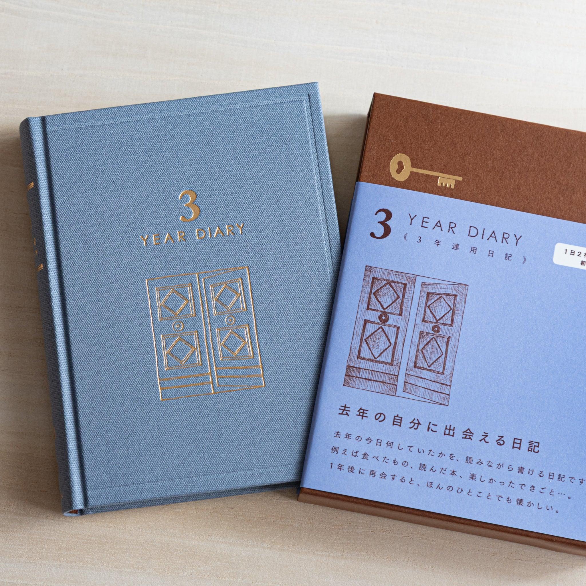 Japanese journal Midori 3-year diary with gray cloth cover and gold gate motif next to brown-blue packaging box