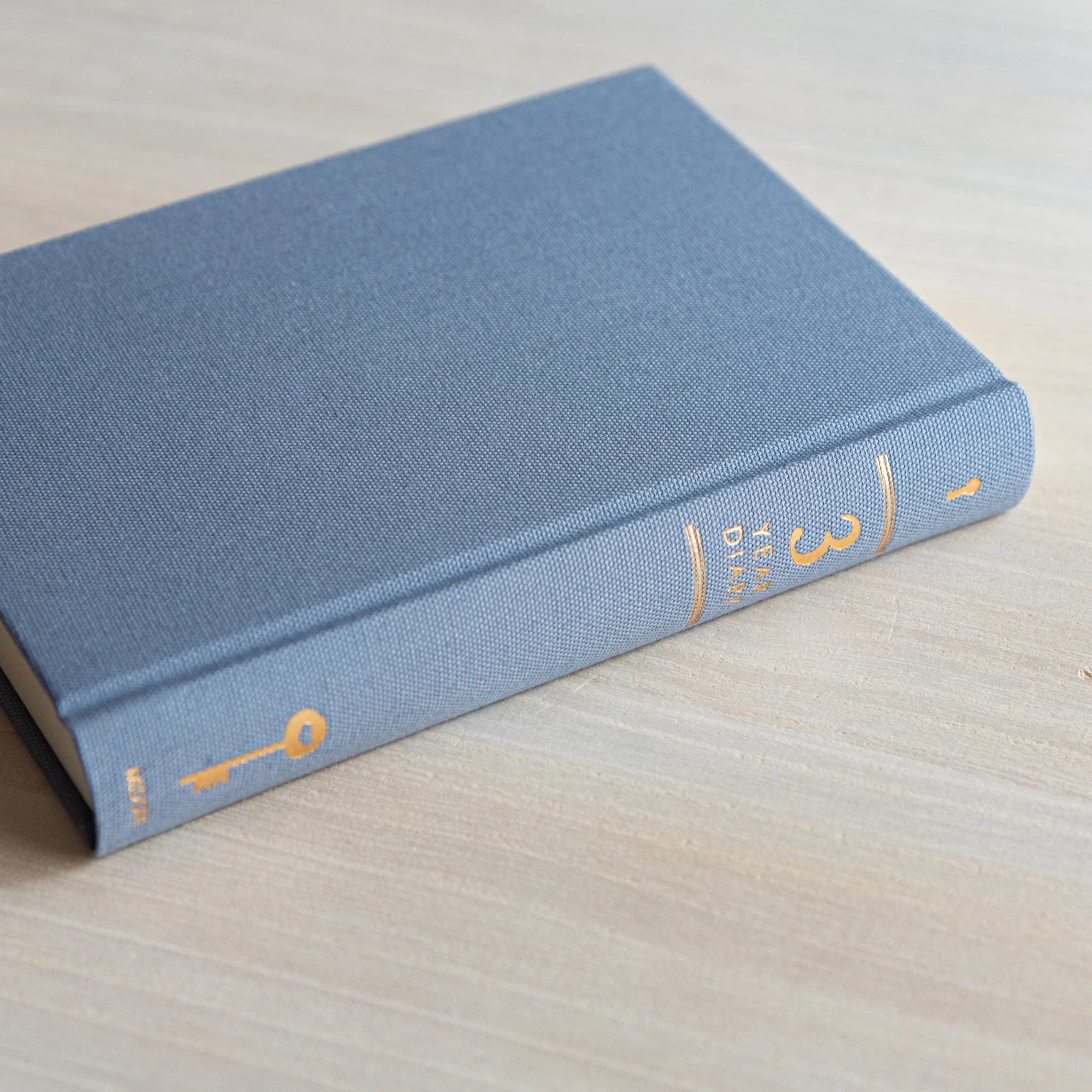 Japanese journal Midori 3-year diary closed blue-gray cover showing spine with golden key and 3 text, side view