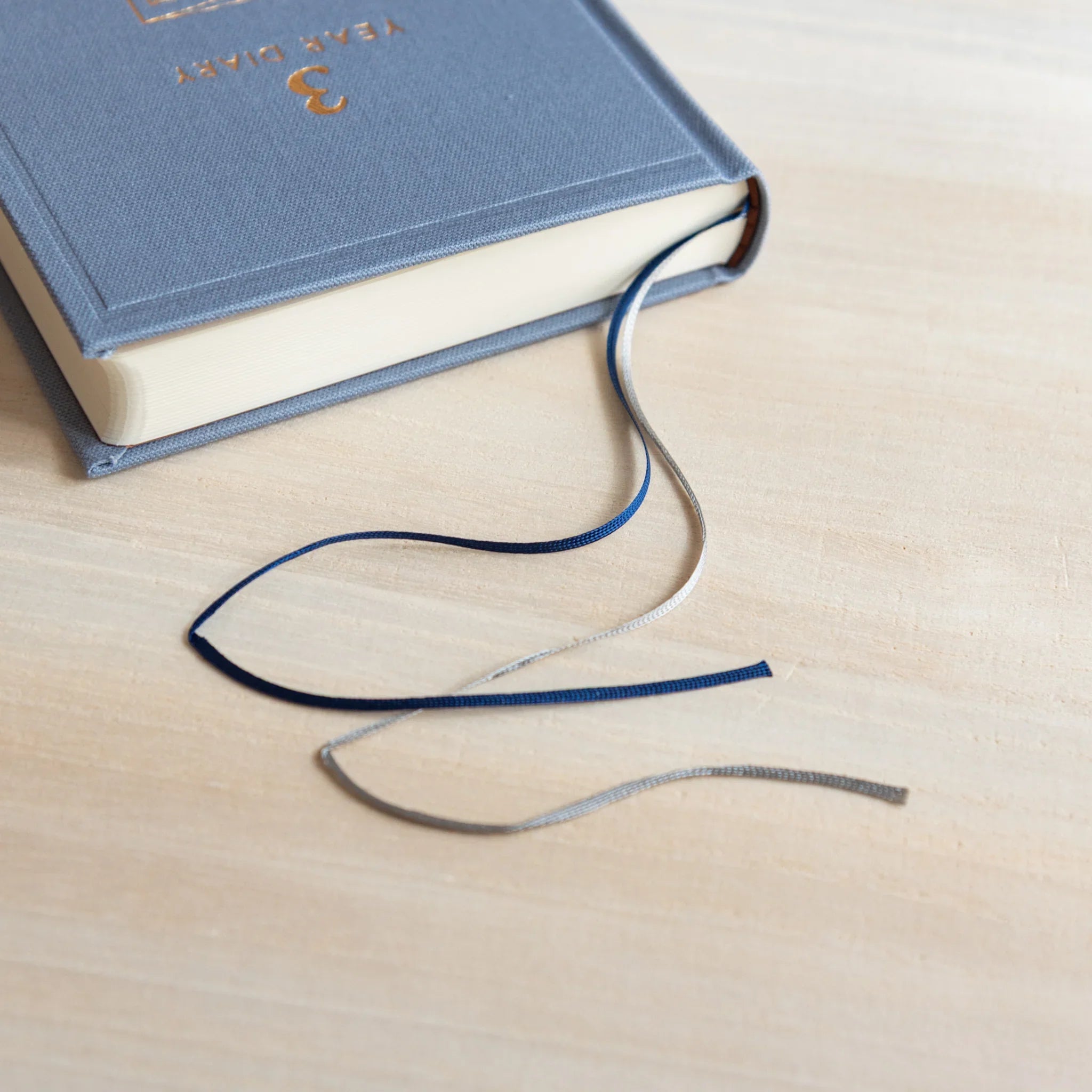 Japanese journal Midori 3-year diary blue book with cream pages and blue and silver ribbon bookmarks looped on desk