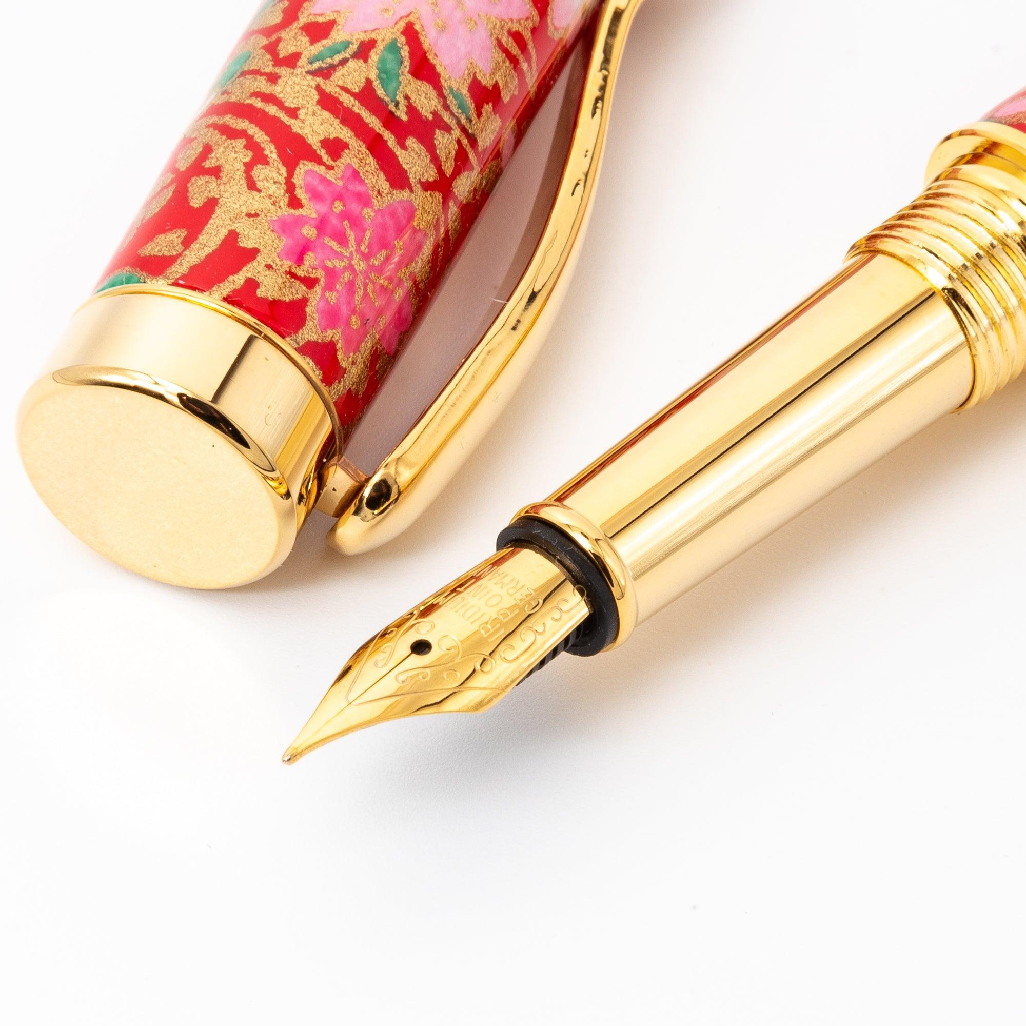 A close-up of a Japanese fountain pen’s gold nib and vibrant red floral barrel design, highlighting its intricate patterns and luxurious craftsmanship.  