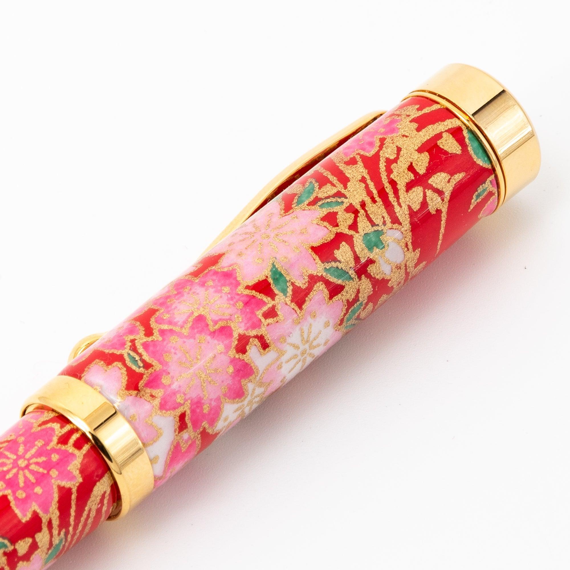 A close-up of a Japanese fountain pen cap with a red floral design and gold details, featuring intricate cherry blossom patterns for a refined look.  