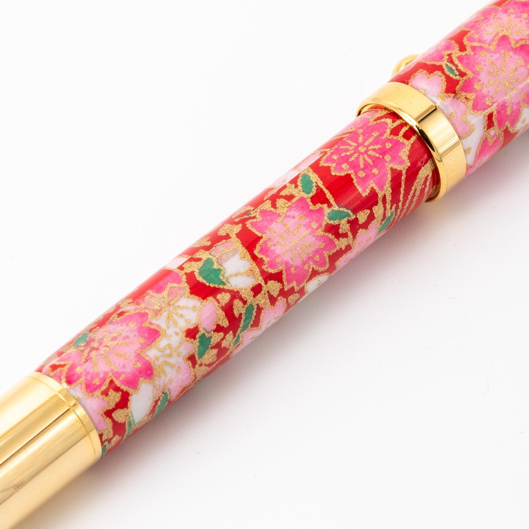 A close-up of the barrel of a Japanese fountain pen with a red floral design, accented by gold trim, showcasing traditional Japanese aesthetics.  