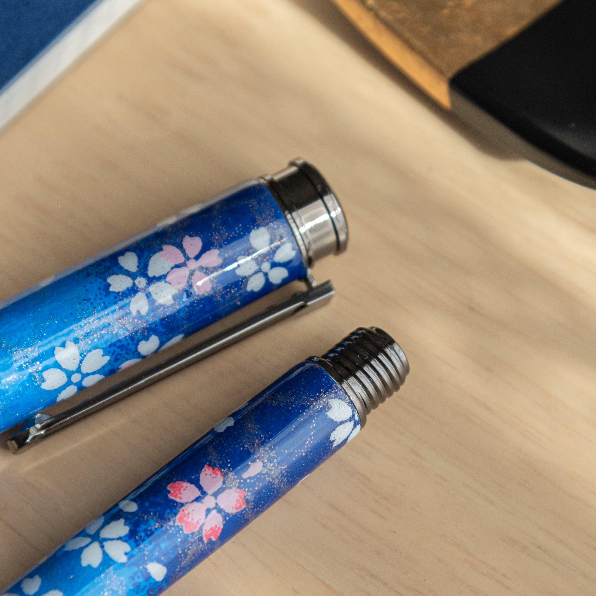 Close-up of Japanese fountain pen cap and barrel with moonlit sakura pattern in blue tones on wooden surface. (95 characters)