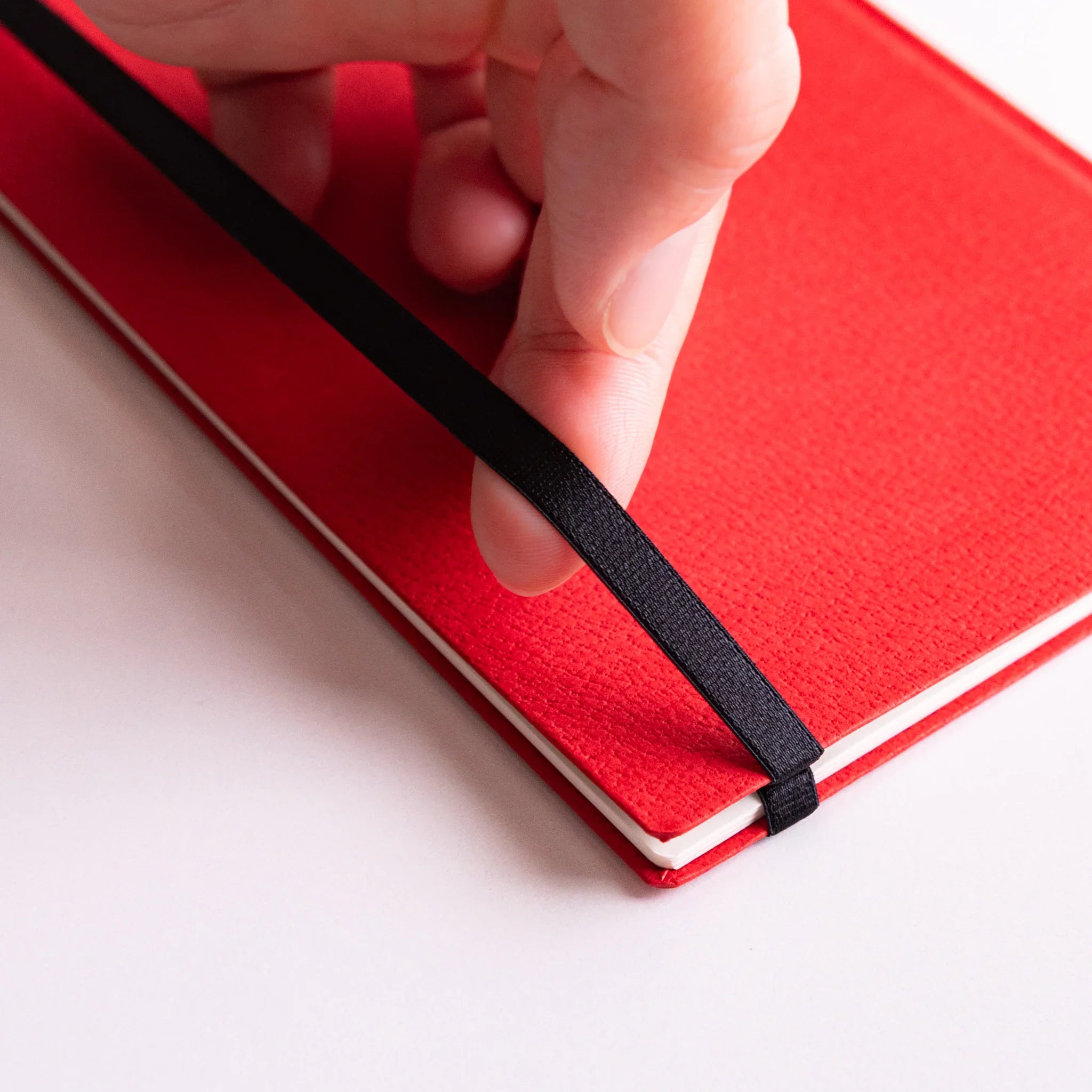 Hand hooking Dressco Sebiro Navy Blue bookmark band strap around corner of red notebook to secure pages.