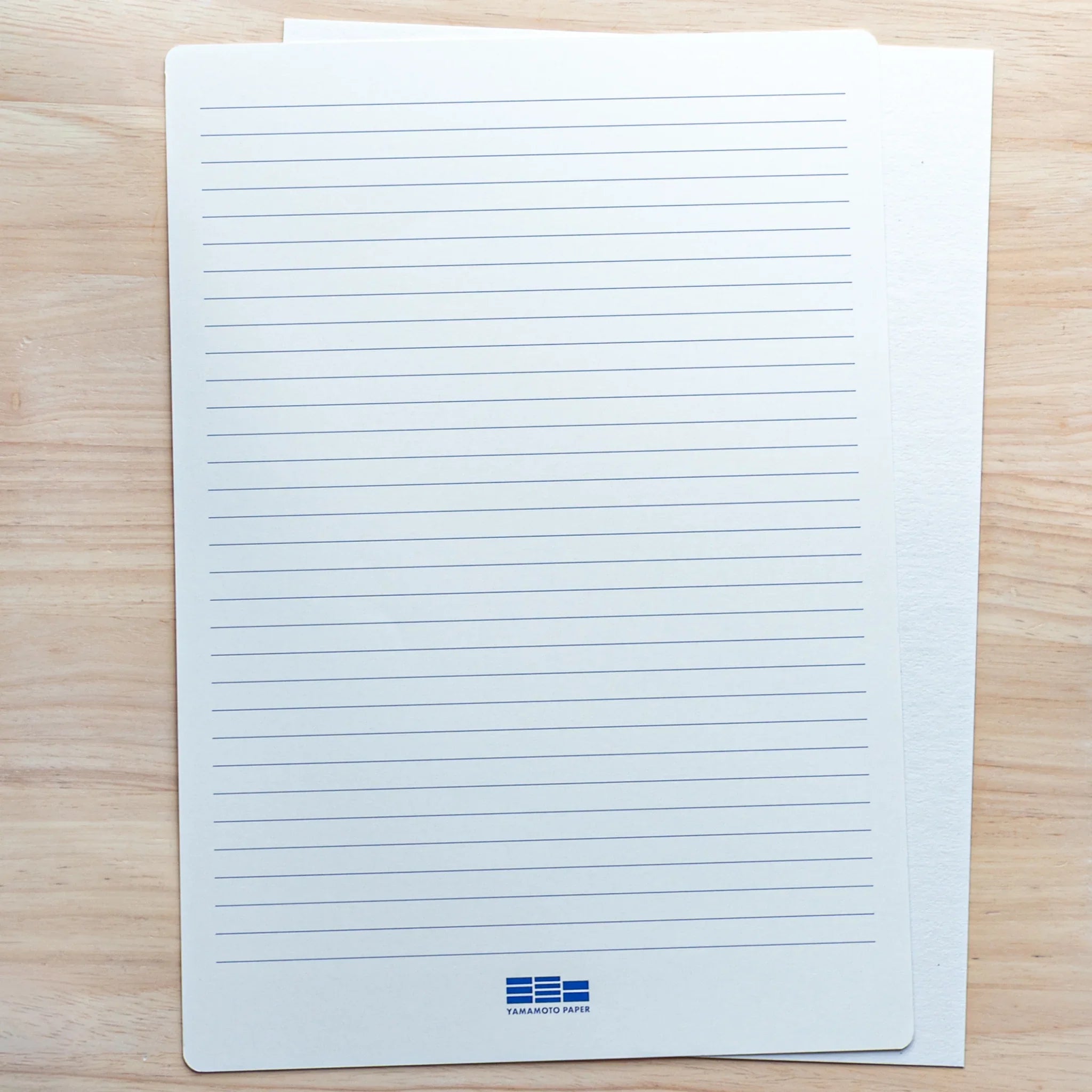 A4 guide sheet printed with blue horizontal ruled lines and the Yamamoto Paper logo, laid over a blank sheet on wood
