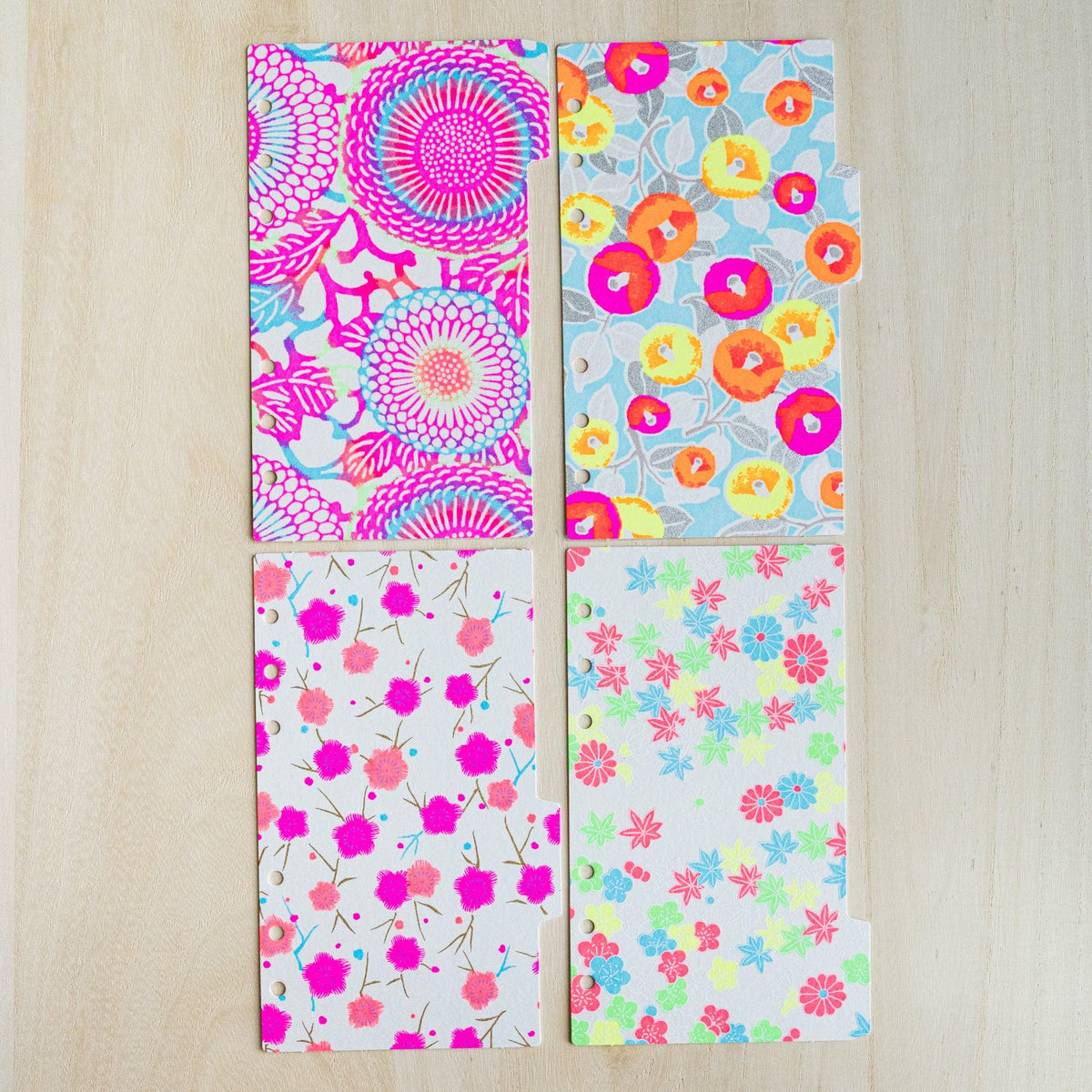 Four neon Yuzen washi index dividers laid in a grid, pink chrysanthemum, blue camellia, plum and maple prints