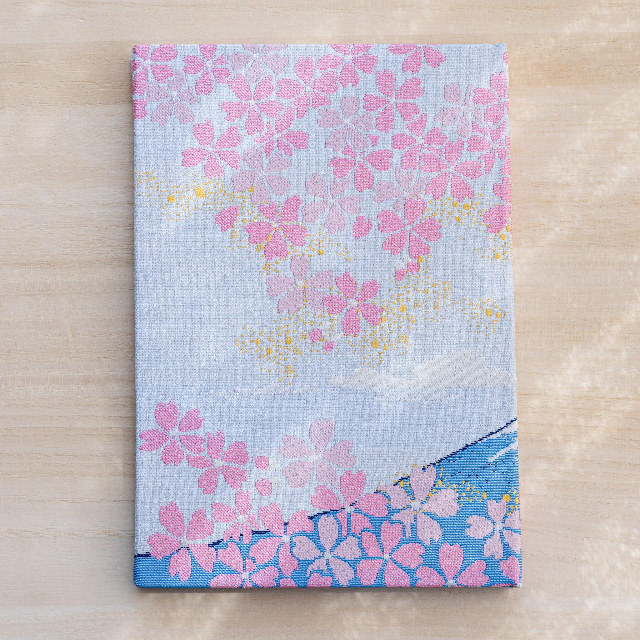Notebook back cover in woven textile, pink cherry blossoms on pale blue with a blue lower band, no Mount Fuji