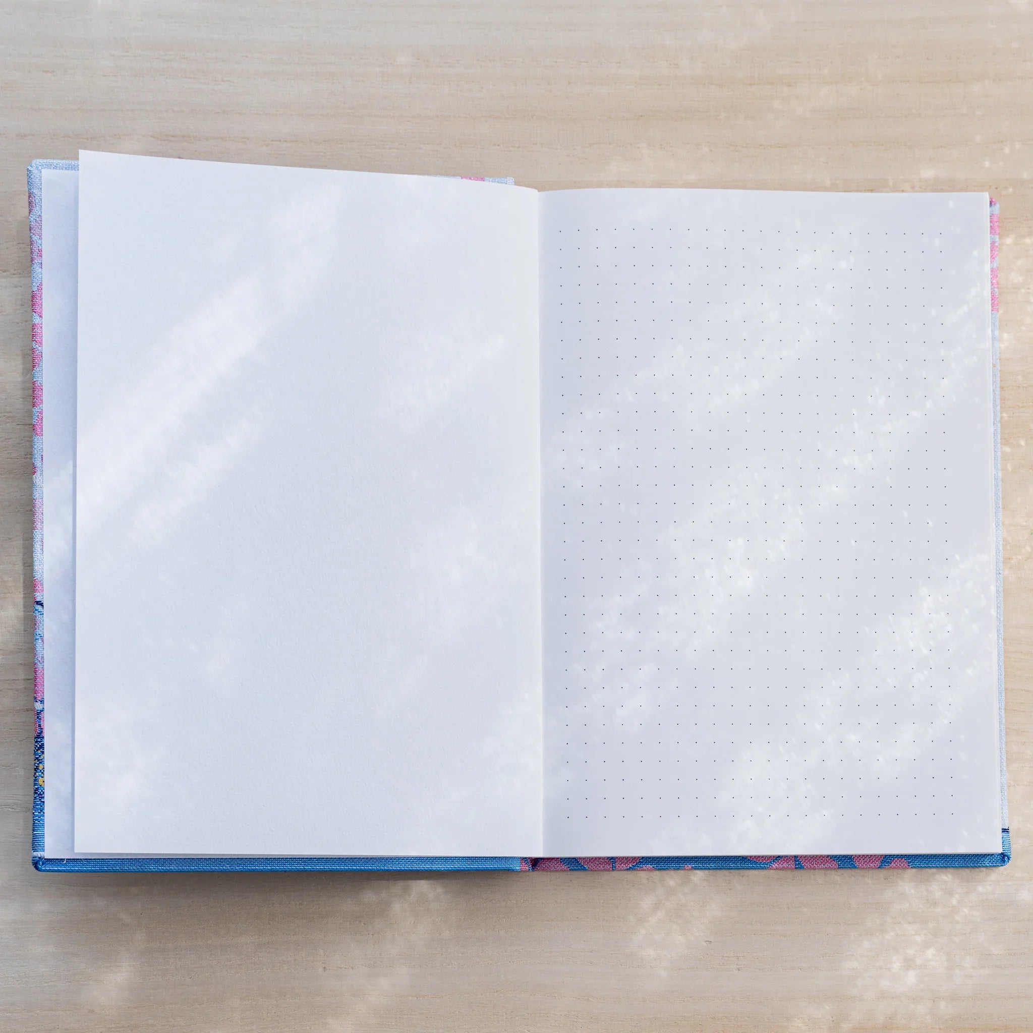 Notebook open showing a blank white page on left and a dot grid page on right, textile cover edges visible