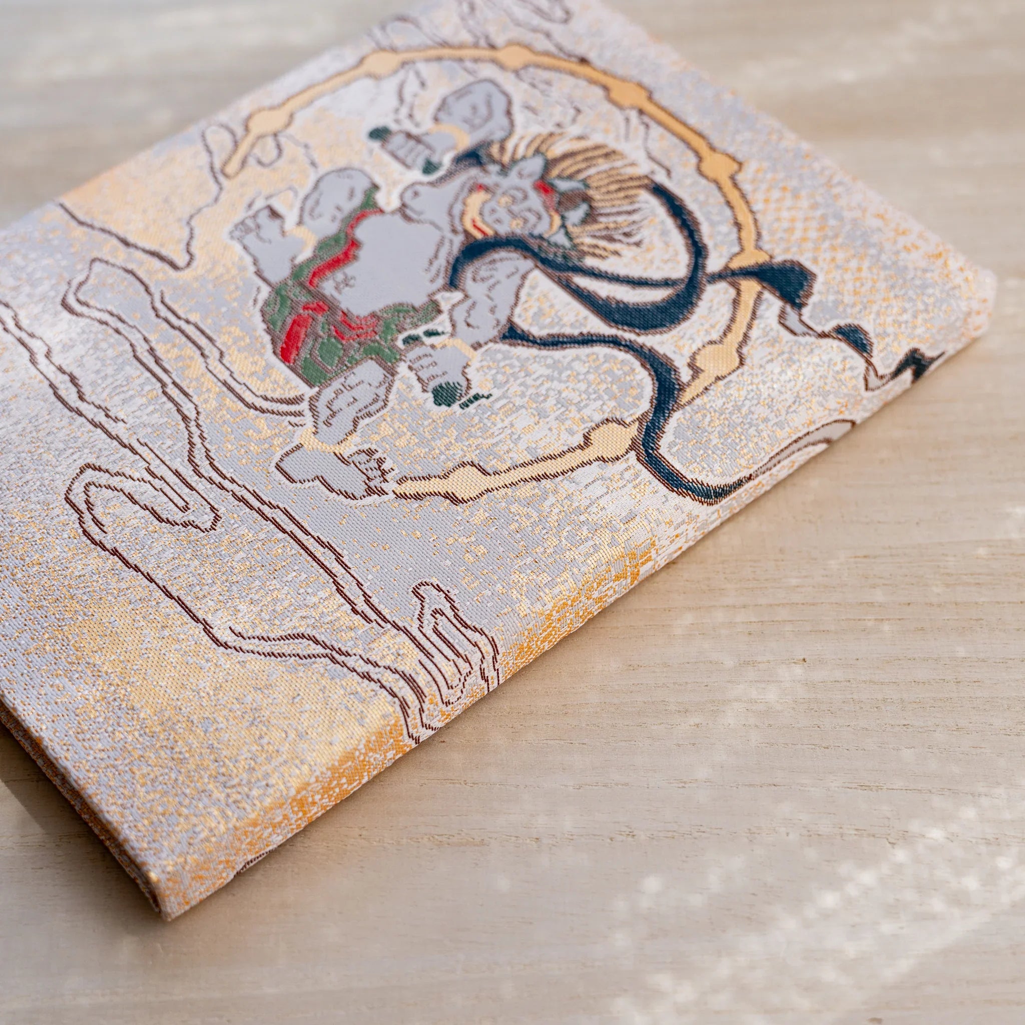 Angled view of notebook back cover, pale thunder god Raijin with a drum ring in woven textile