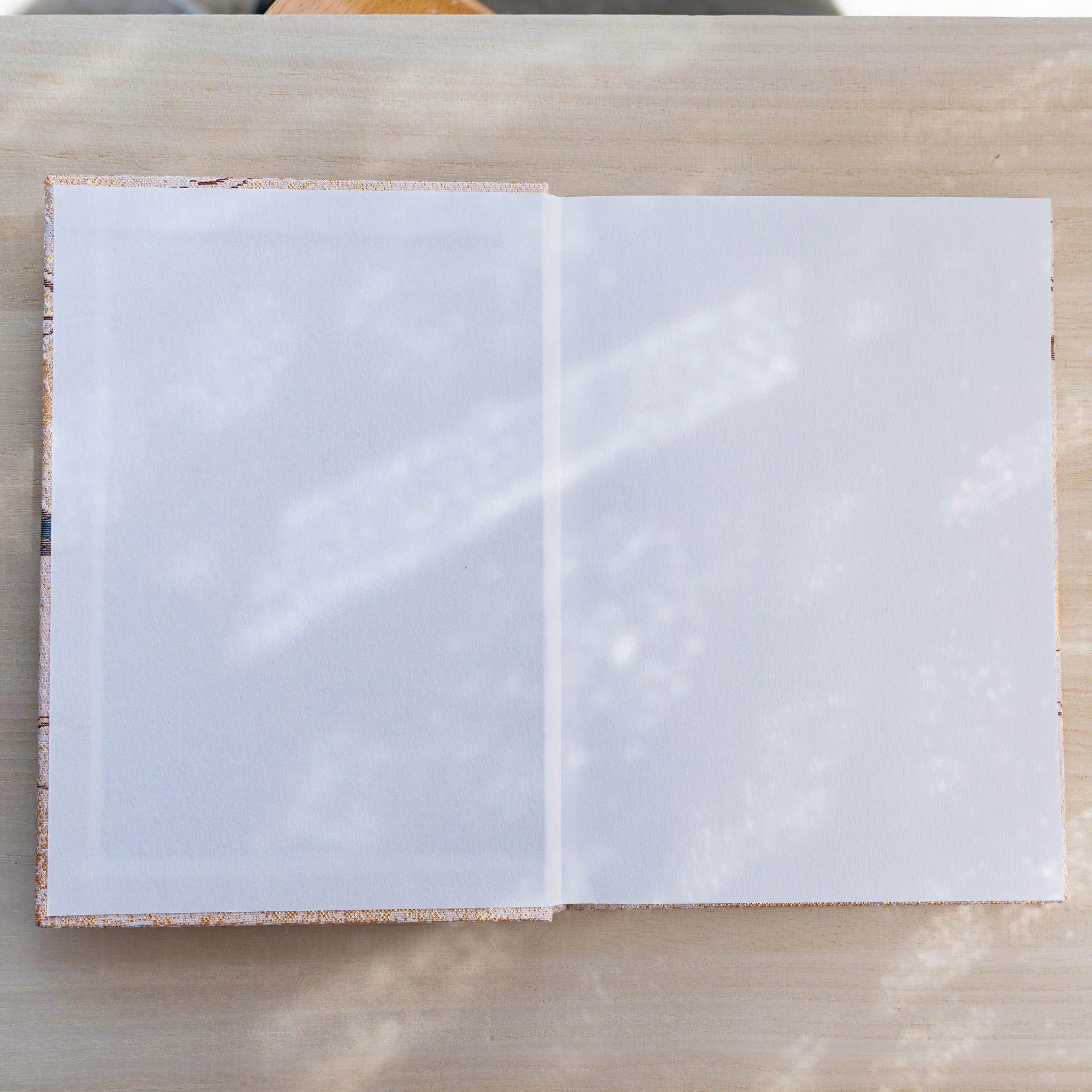 Notebook opened flat to two blank white pages, gold patterned textile inner cover visible at the edges