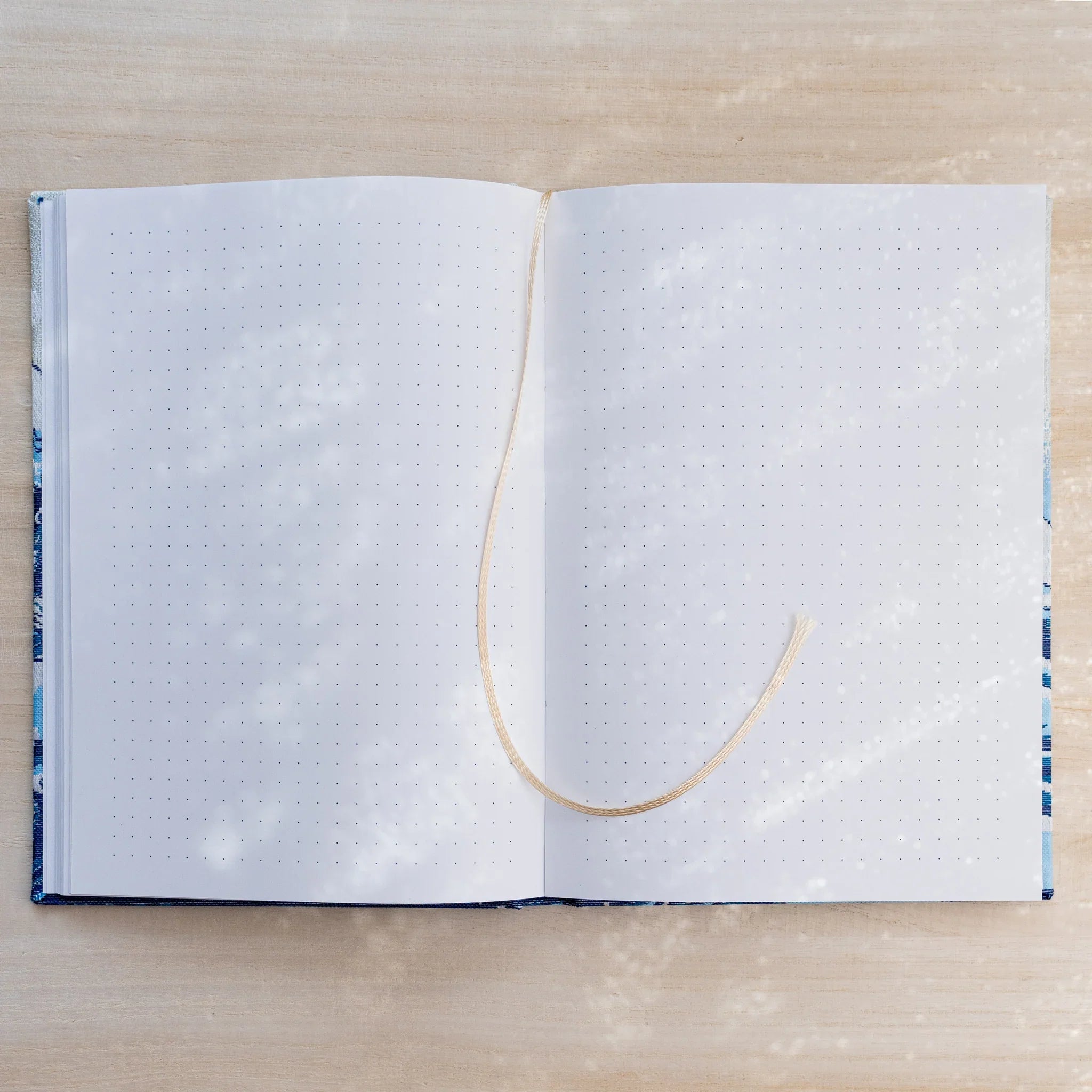 Notebook open flat to dot grid pages on both sides with a beige ribbon bookmark, blue textile cover edges