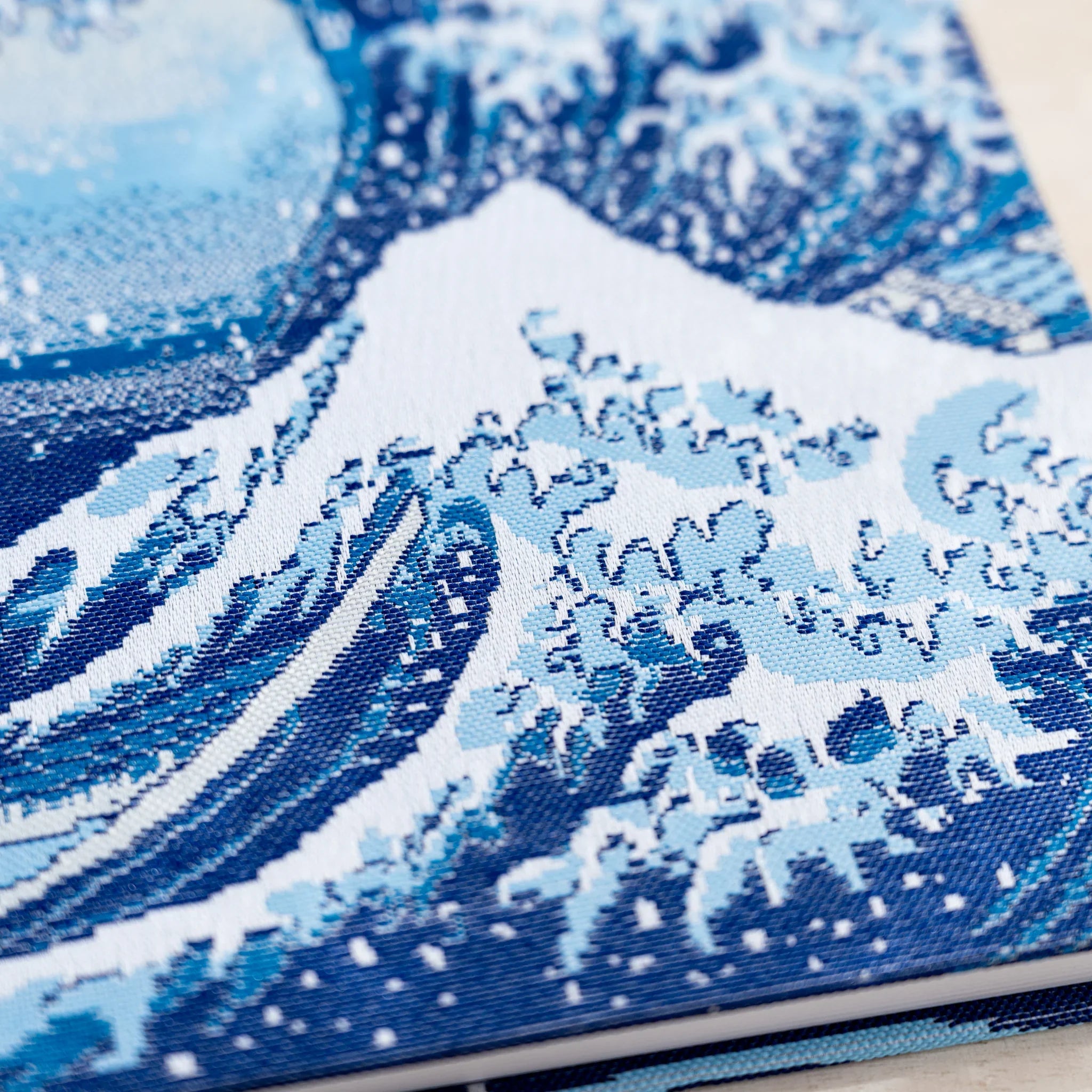 Close-up of woven textile wave in shades of blue with white foam and dotted spray