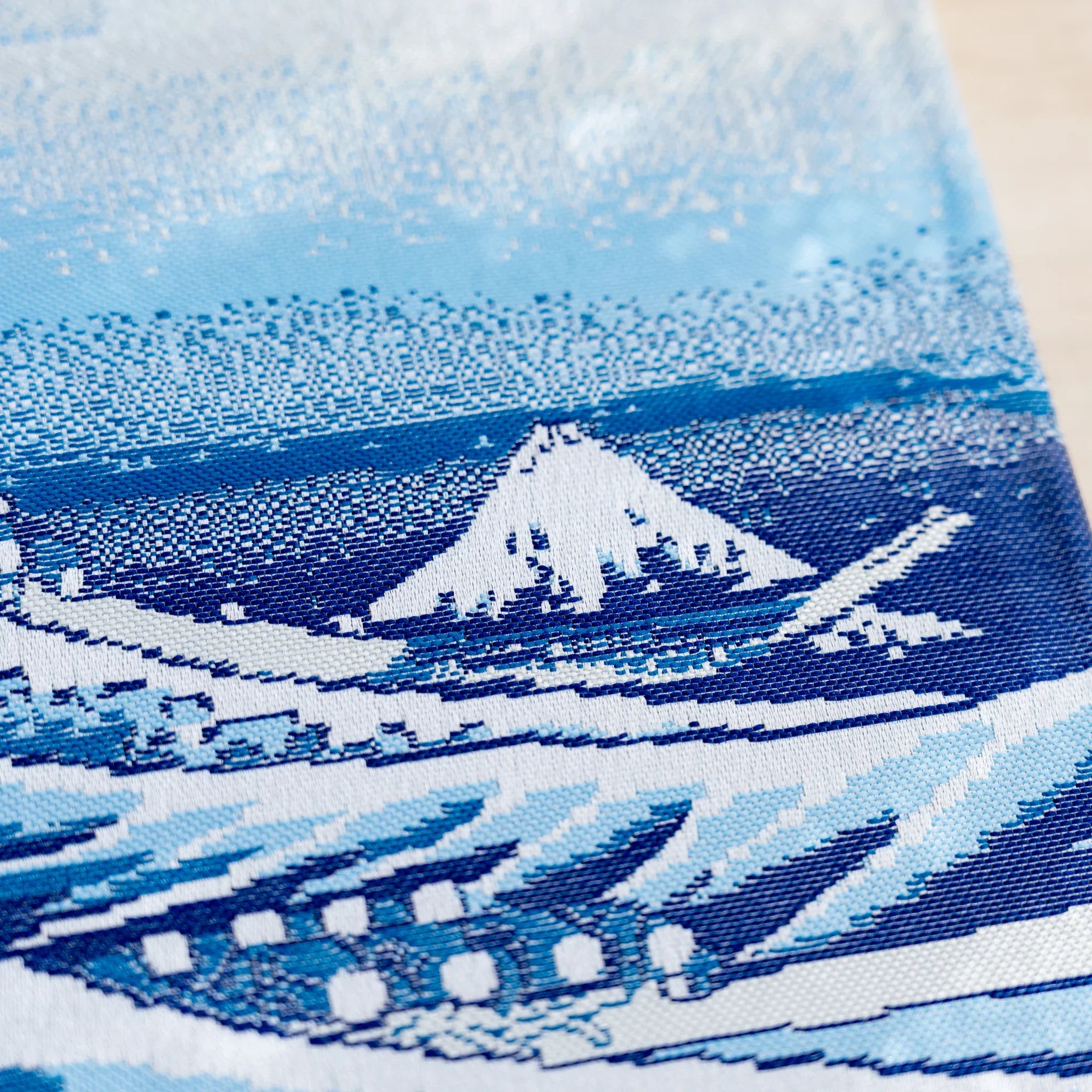 Close-up of woven textile with small Mount Fuji, blue waves, and rows of small white shapes