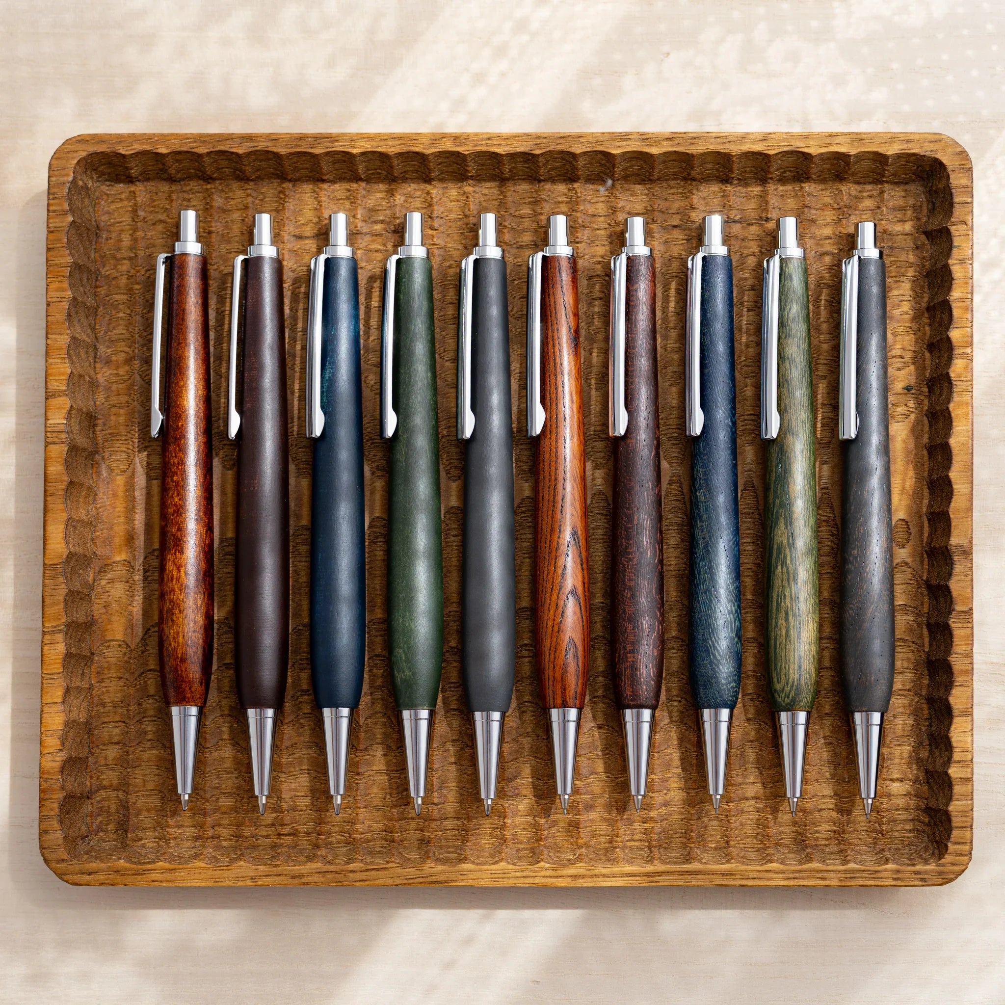 Ten NIVI urushi lacquered mechanical pencils in five colors laid in a carved wooden tray, Japanese keyaki wood